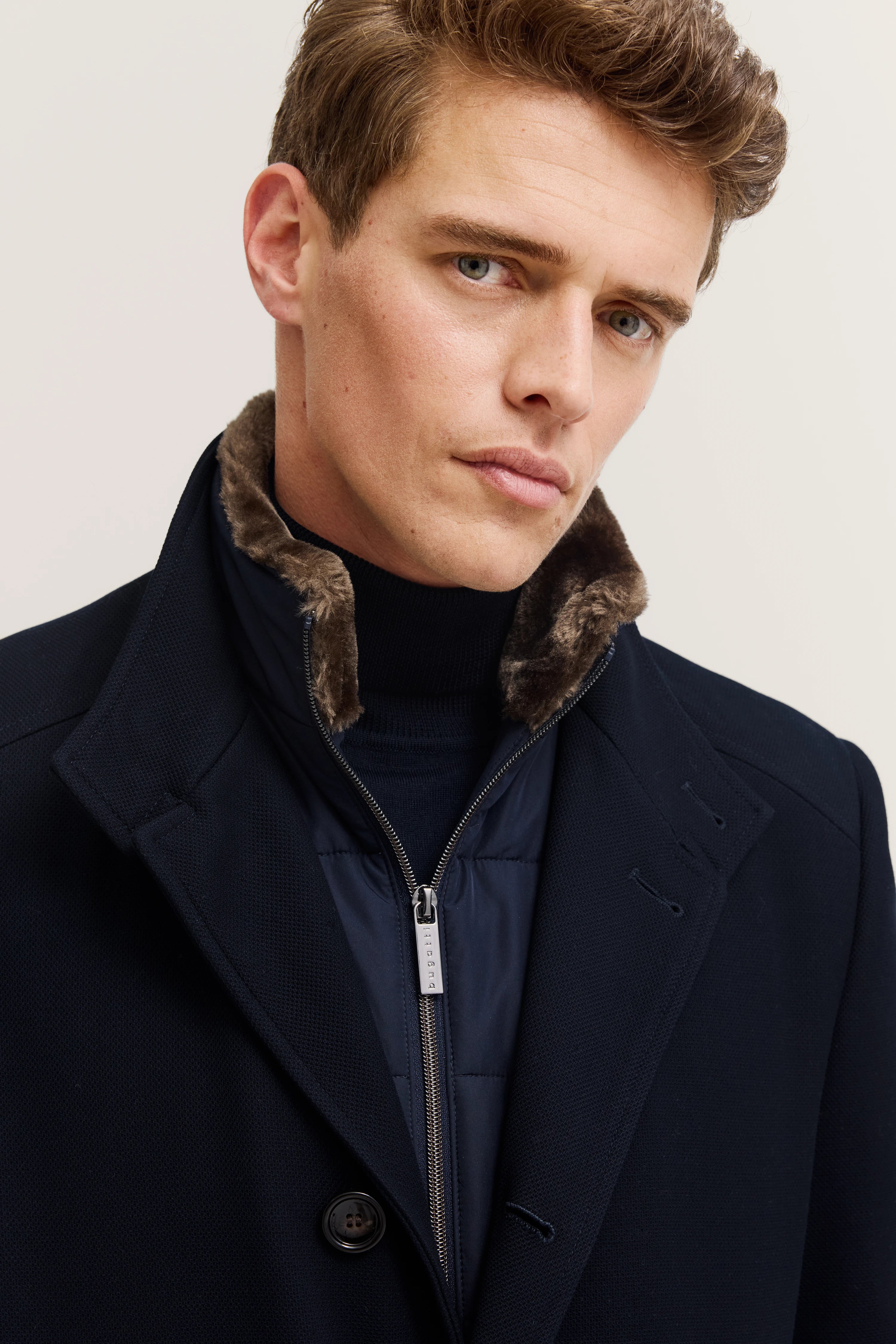 Bugatti Herrenmodel in dunklem Mantel mit Fellkragen, legeres Posing.