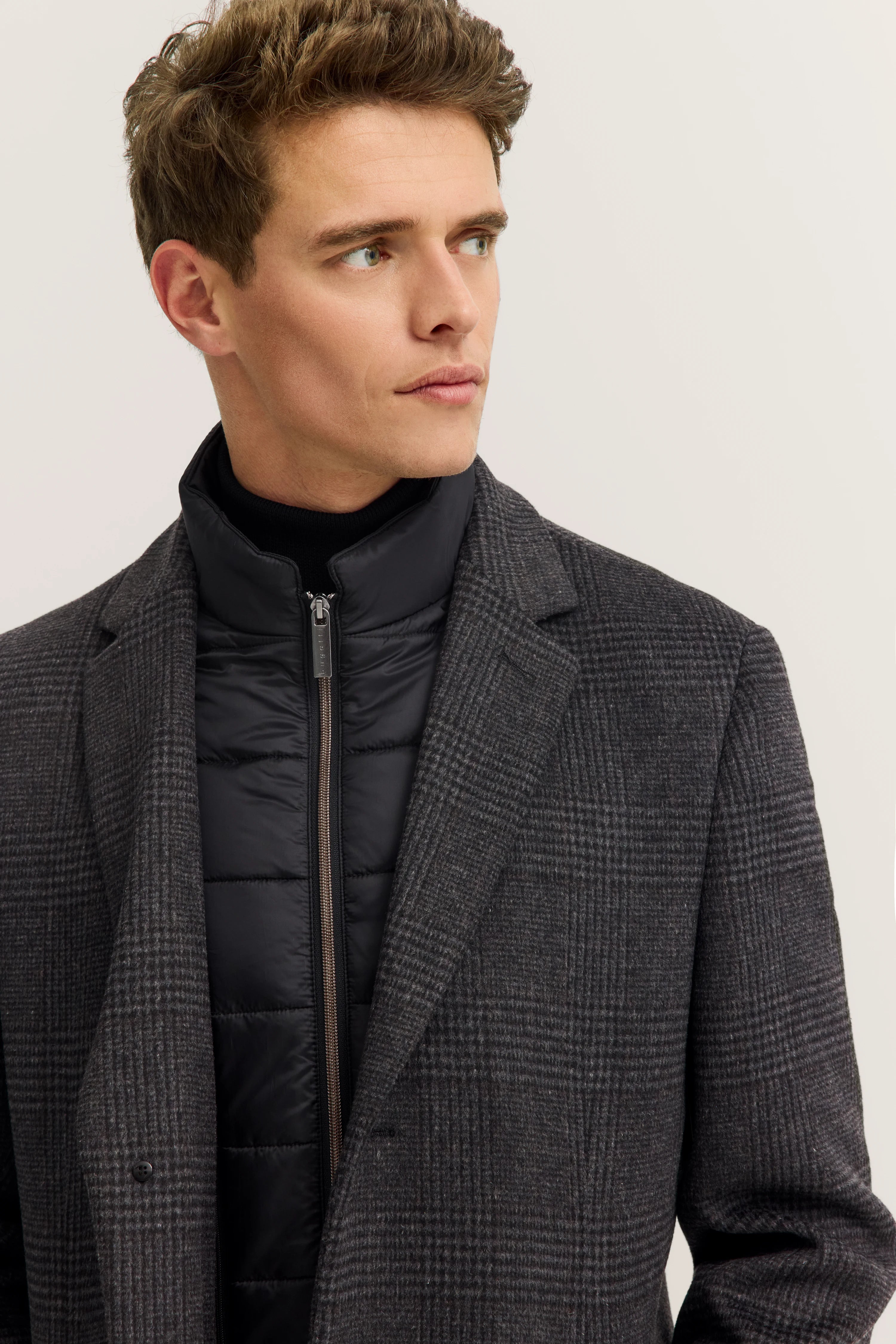 Grauer Glencheck-Mantel und schwarzer Steppjacke von bugatti, Büstenbild.