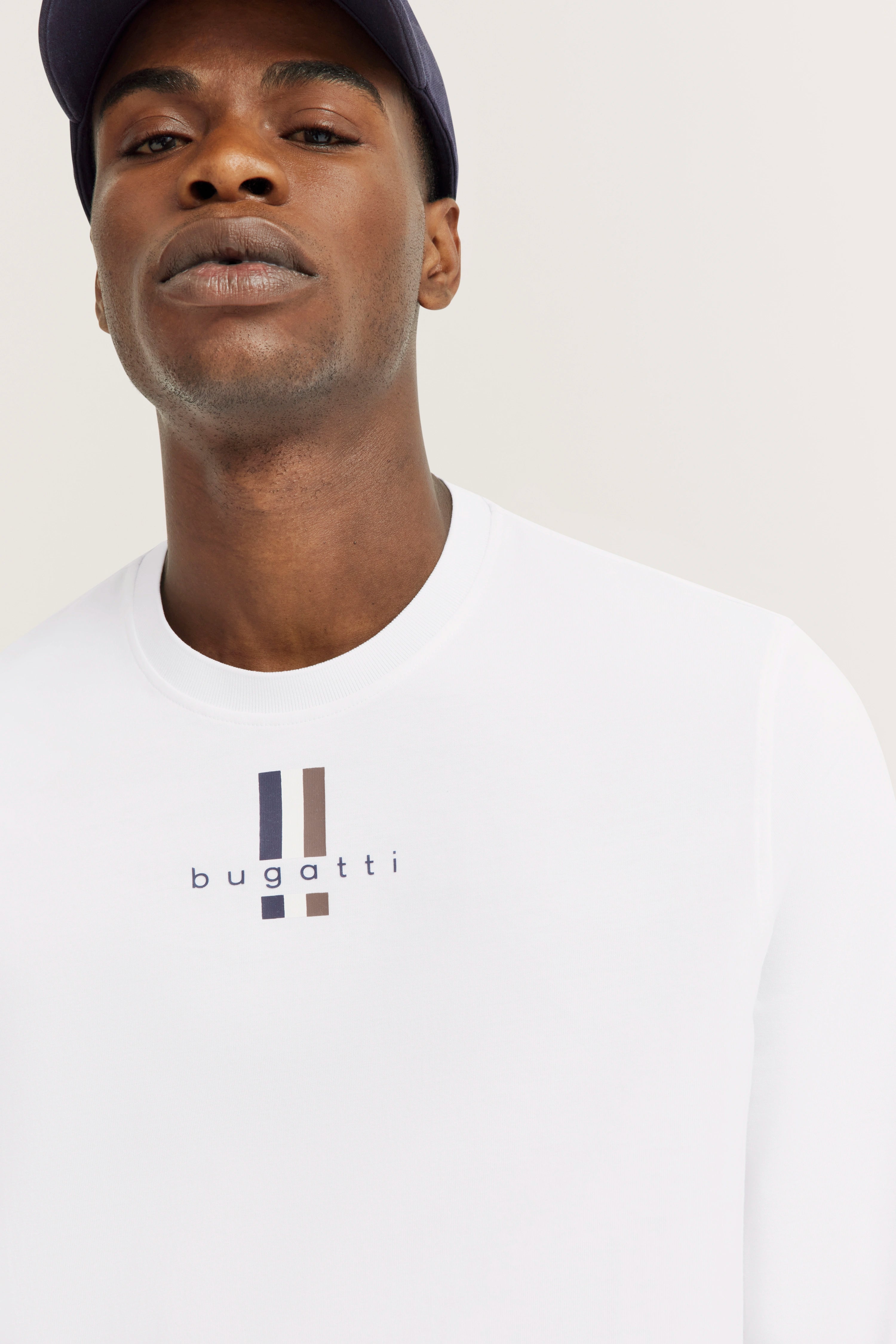 White bugatti sweatshirt with logo, model posing casually, wearing dark baseball cap.