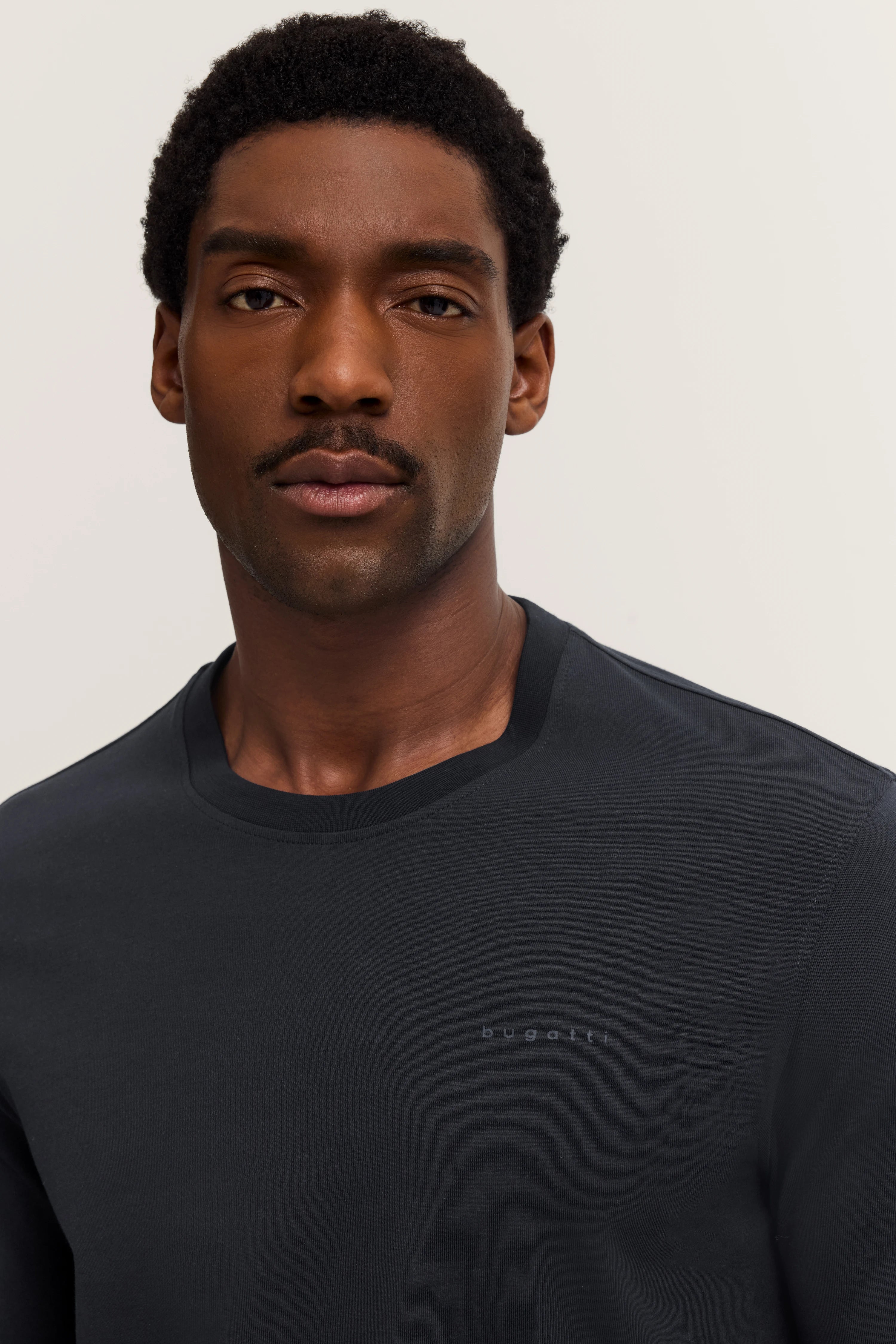 Alt-Text: Model mit schwarzem bugatti Pullover, frontal, schlichtes Design, dezentes Logo, stilvoll und zeitlos.