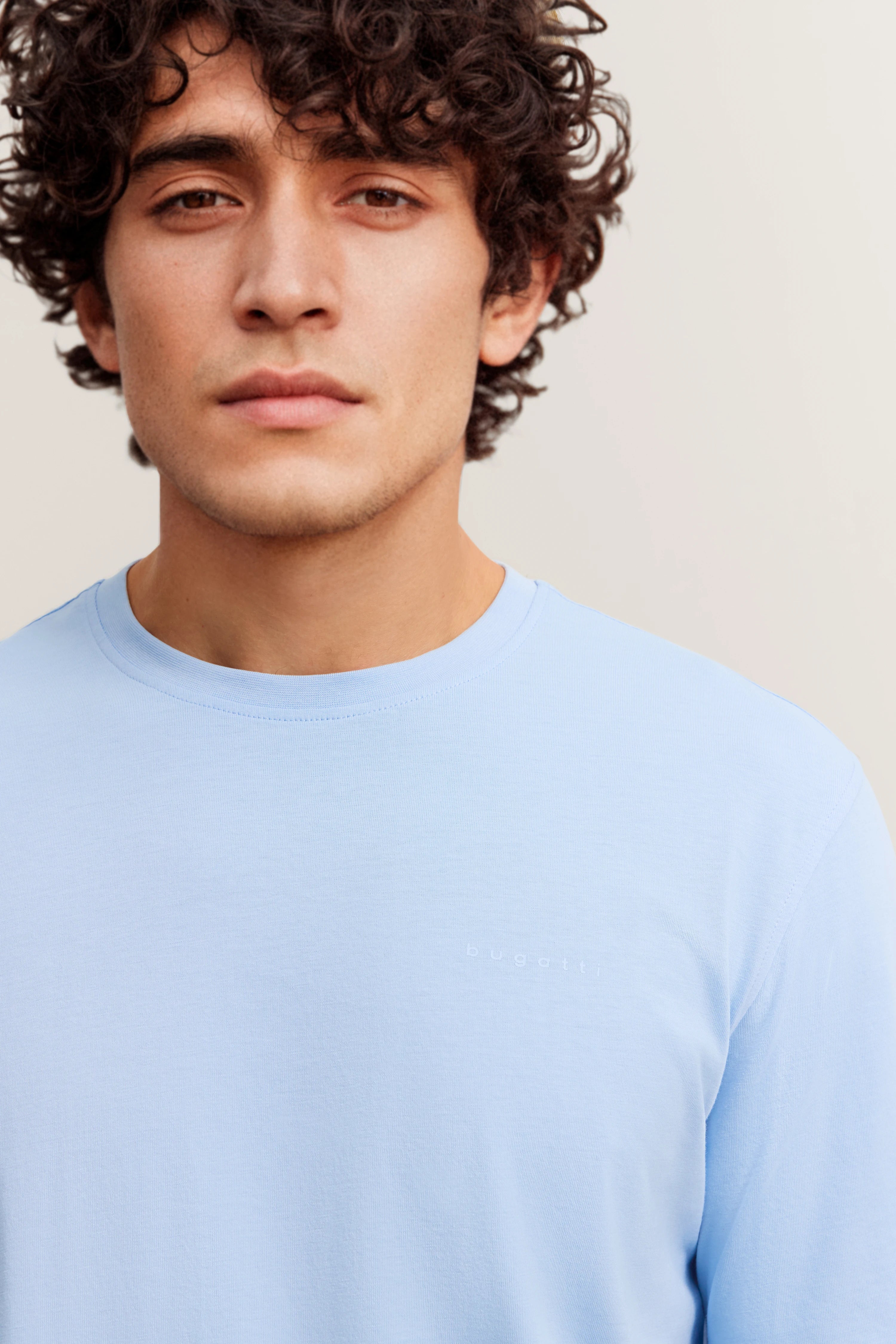 Bugatti Modelbild, hellblaues Shirt, entspanntes Posing, stilvoll und zeitlos.