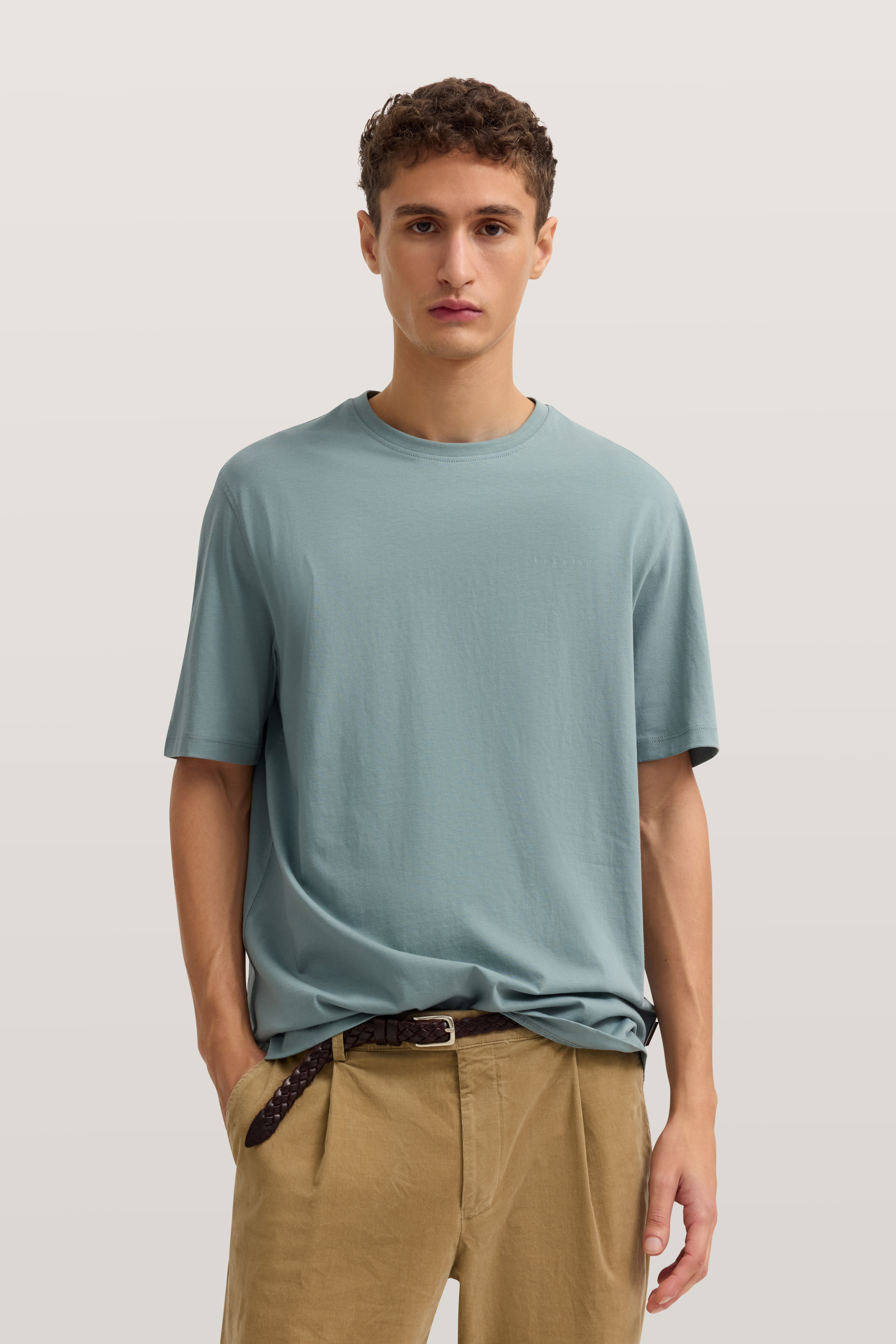 Model in blauem T-Shirt und beigen Hose, entspannte Pose.