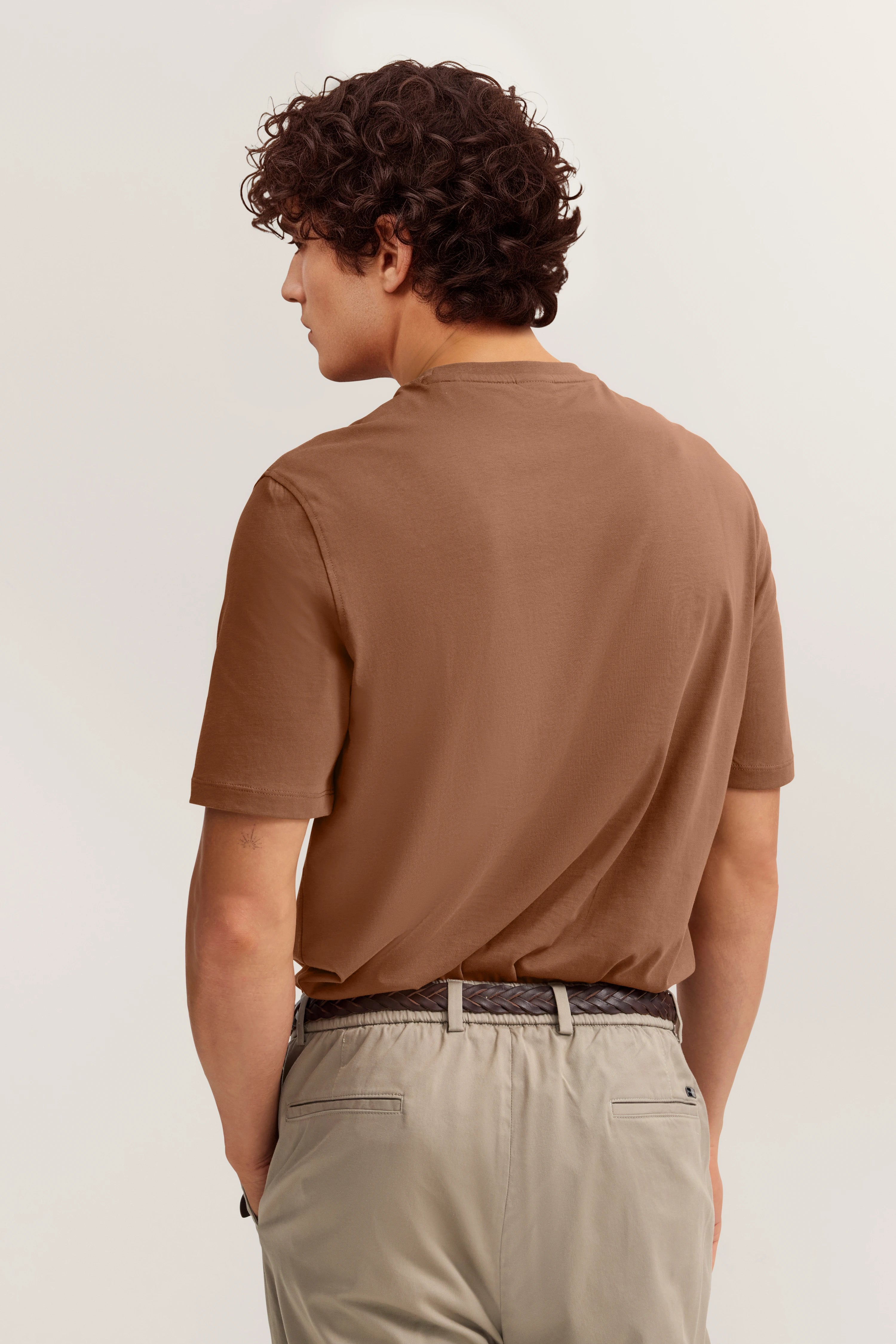 Braunes T-Shirt und beige Hose von hinten, Model blickt zur Seite, entspannte Pose.