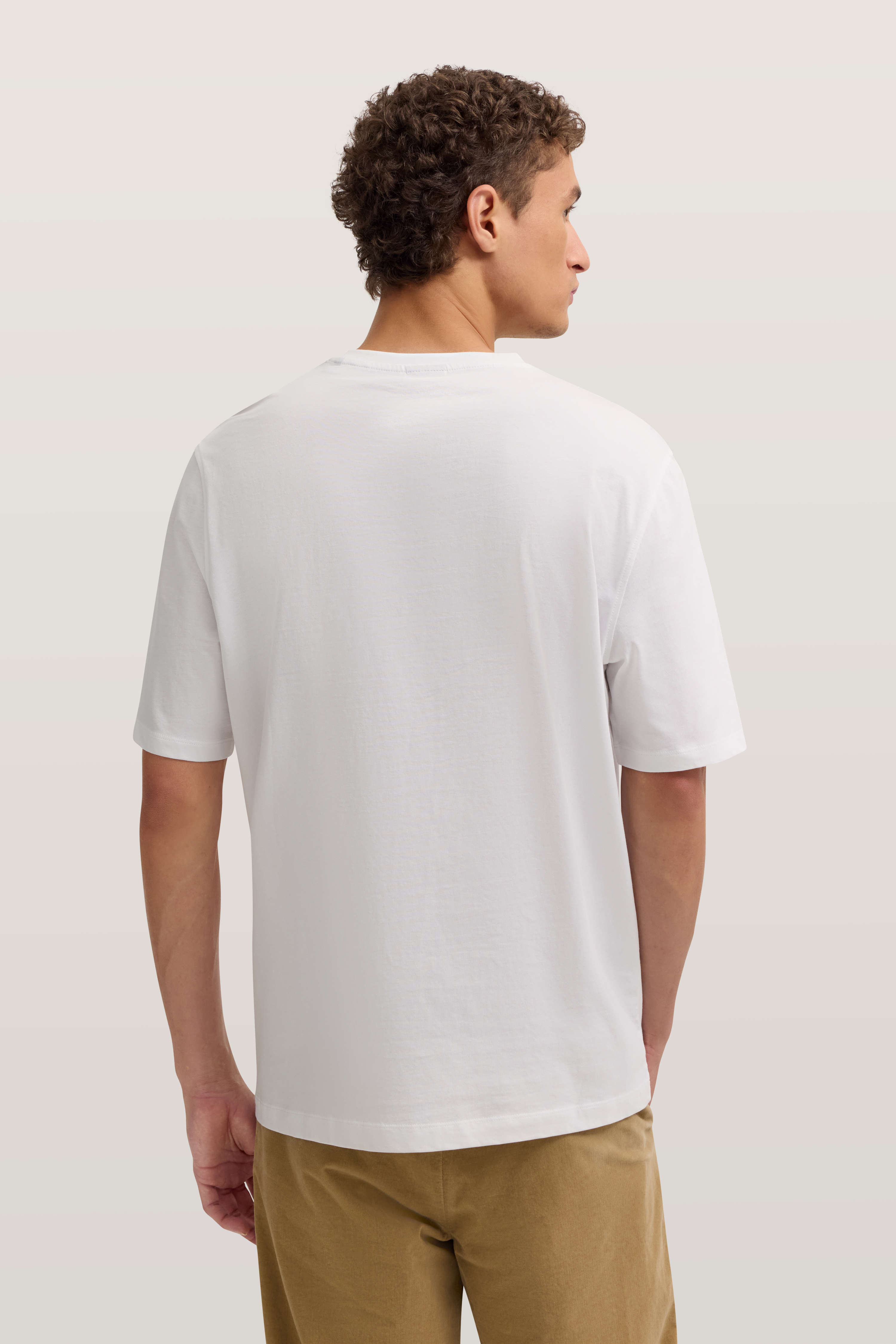 Weißes T-Shirt und beige Hose, Model von hinten, entspannte Haltung.
