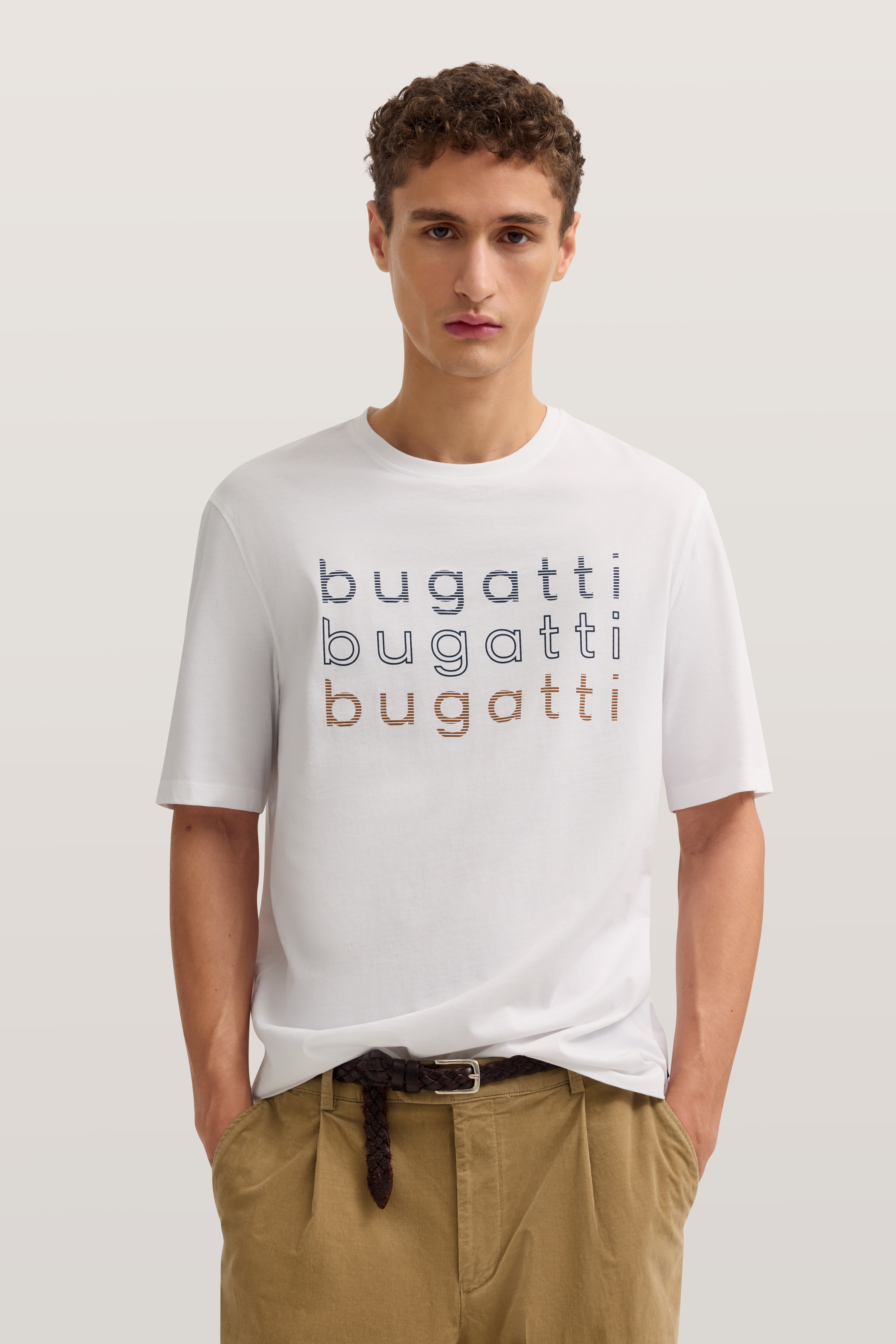 Weißes bugatti T-Shirt mit Logo, beigefarbene Hose, Modelbild, entspanntes Posing.