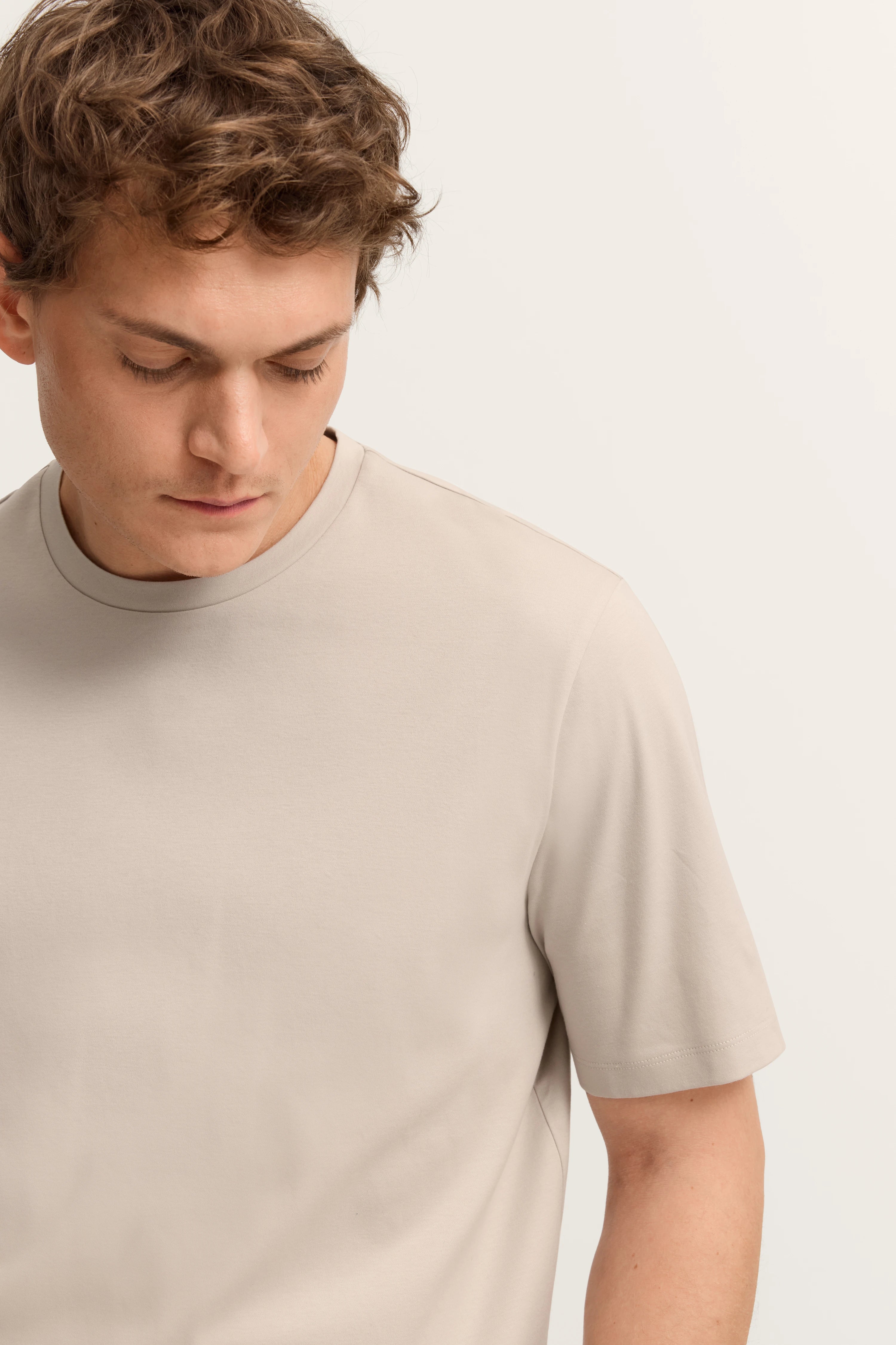 Bugatti Modelbild: Mann in beige T-Shirt, Kopf leicht gesenkt, entspannter Look.