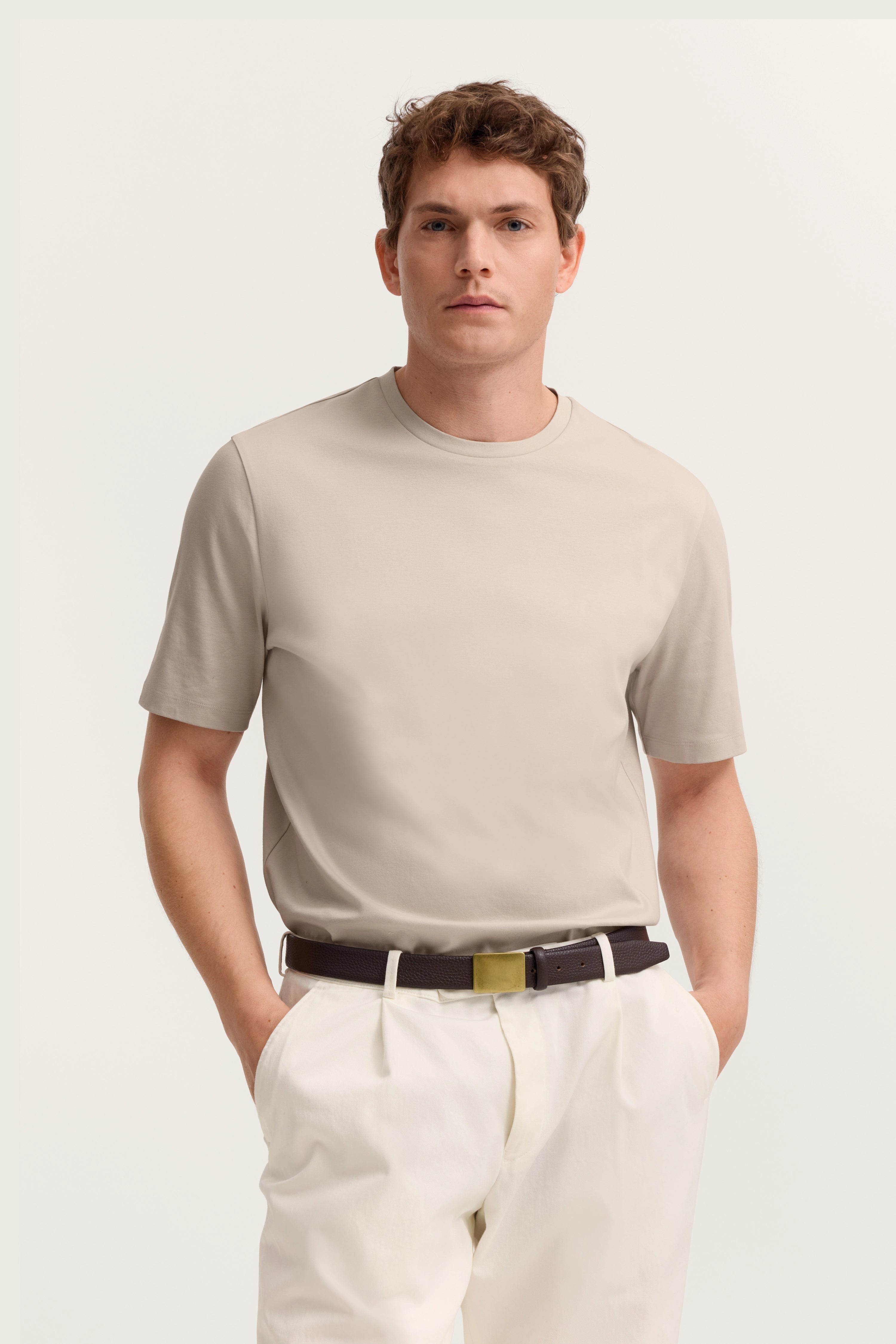 Beiges T-Shirt und weiße Hose, Modelbild, Hände in den Hosentaschen, entspannte Pose.