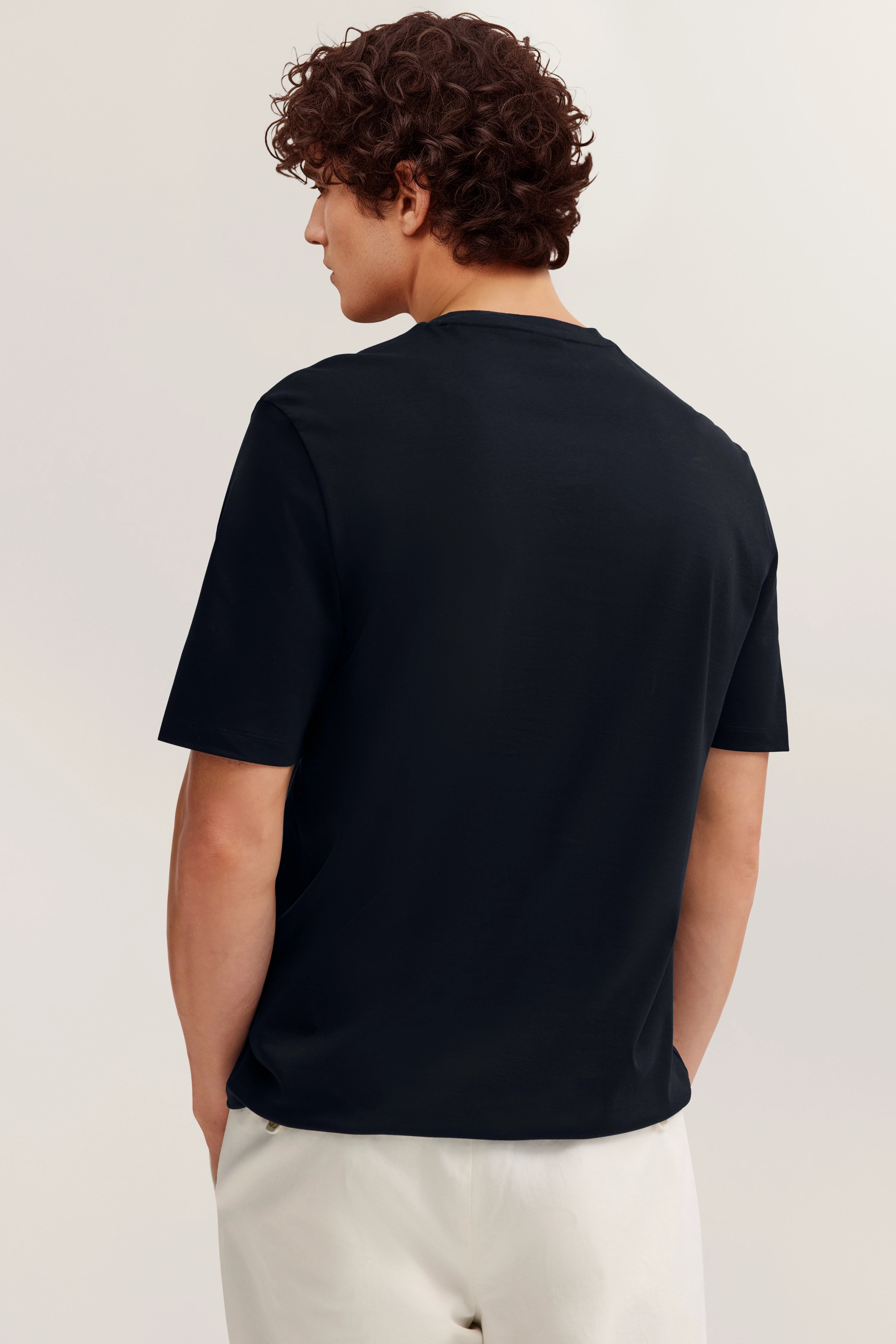 Modelbild: Mann in schwarzem bugatti T-Shirt und weißen Hosen, Rückenansicht, entspanntes Posing.