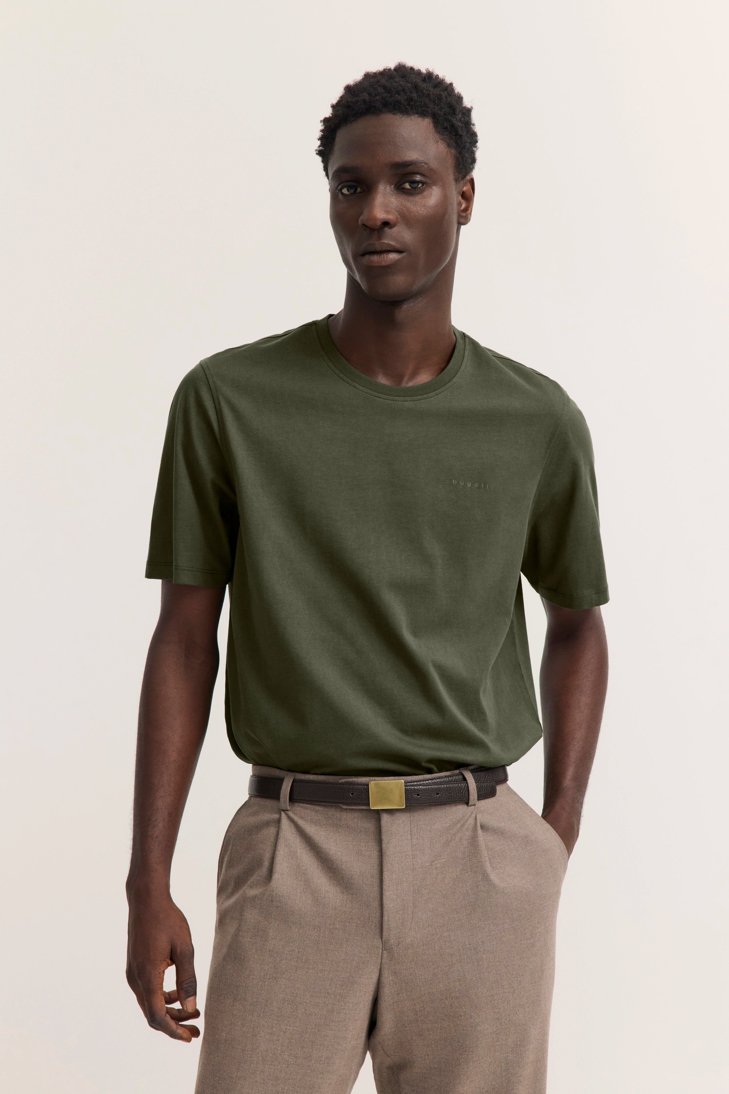 "bugatti Modelbild, olivgrünes T-Shirt, beige Hose, lässige Pose, zeitloser Stil."