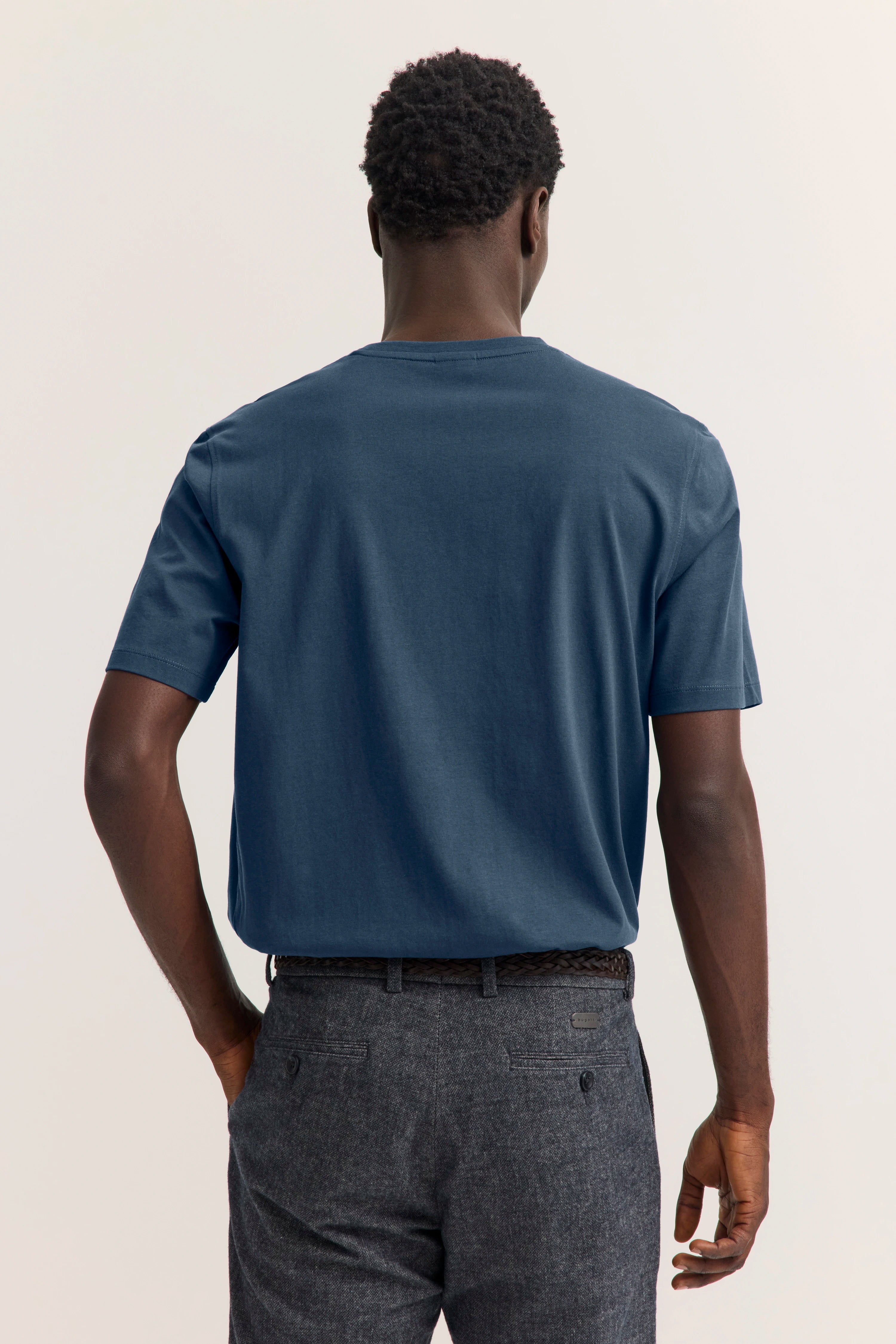 bugatti Modelbild: Mann in blauem T-Shirt und grauer Hose, Rückansicht, legeres Posing.