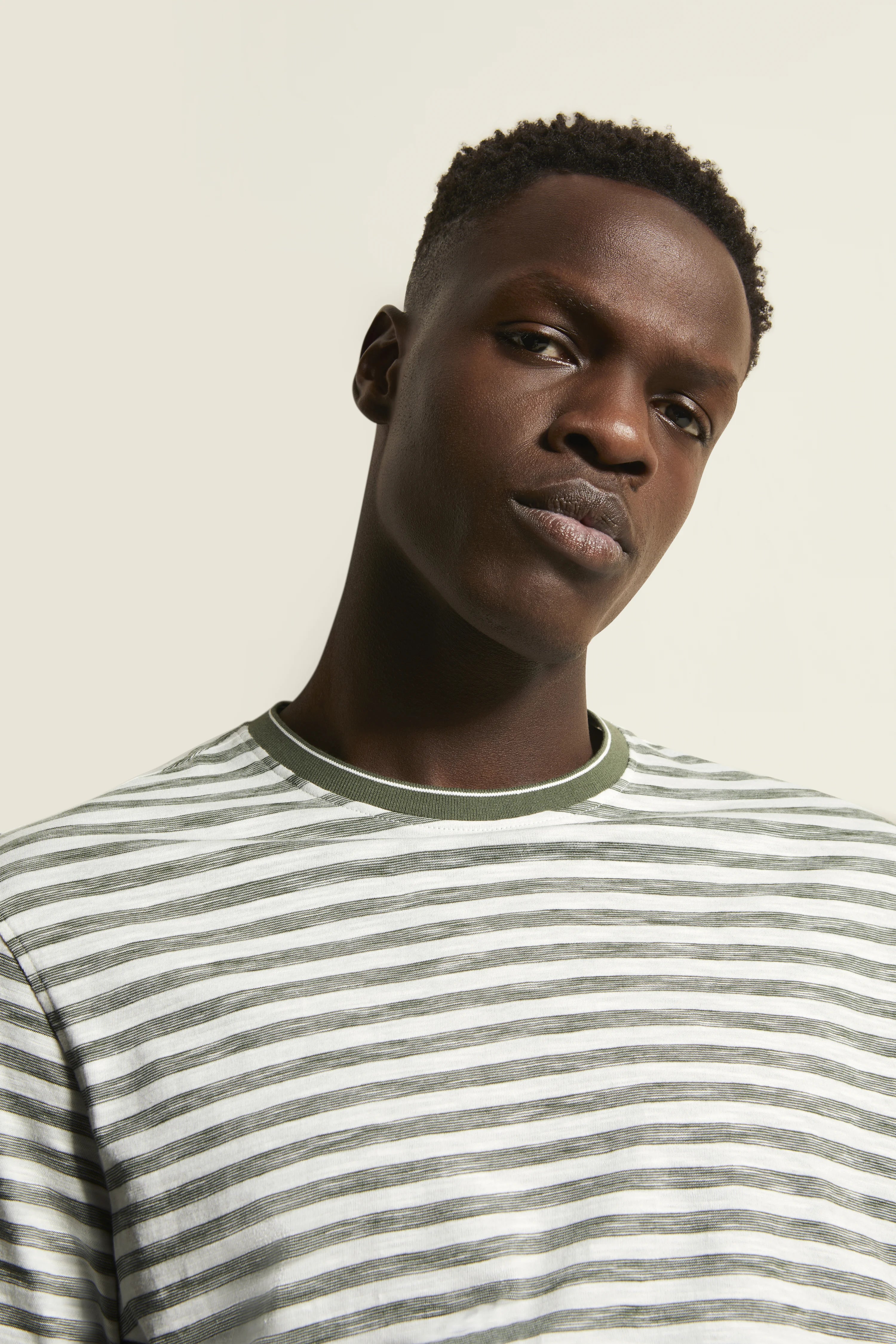 Model in a striped bugatti shirt, white and green, casual portrait with a relaxed expression.