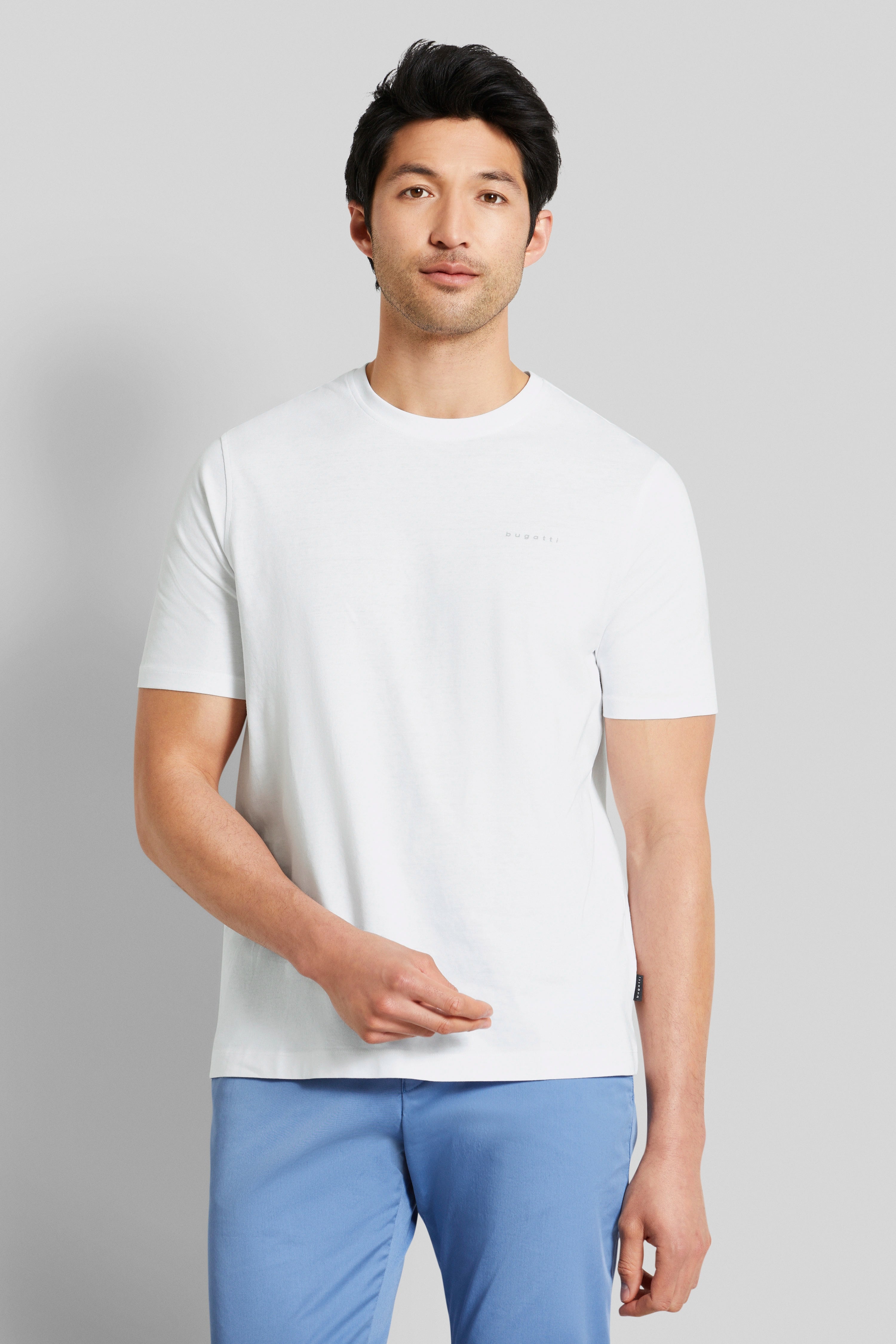 White bugatti T-shirt, blue pants, model in relaxed pose.