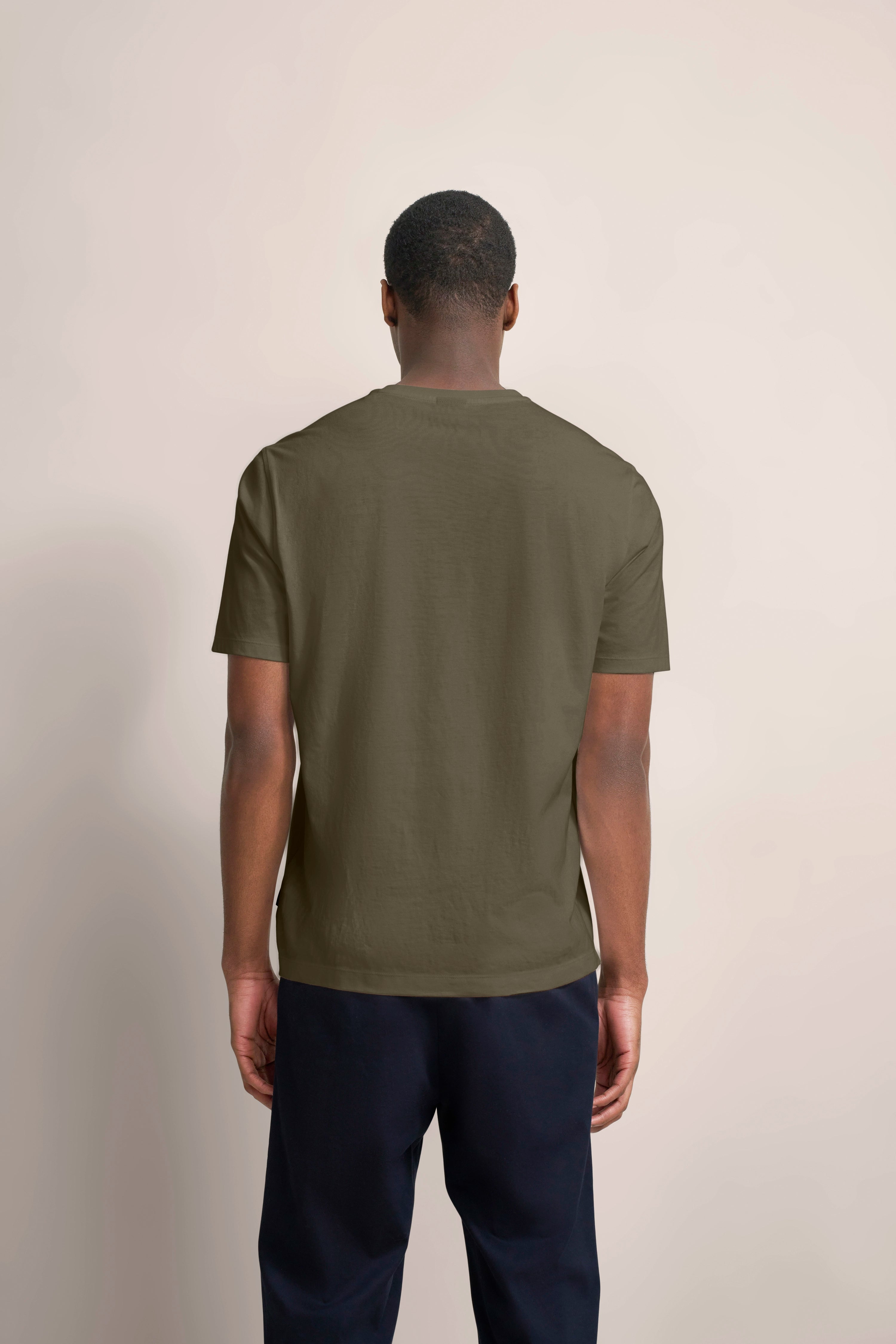Rückansicht eines legeren Outfits mit olivgrünem T-Shirt und dunkelblauer Hose.