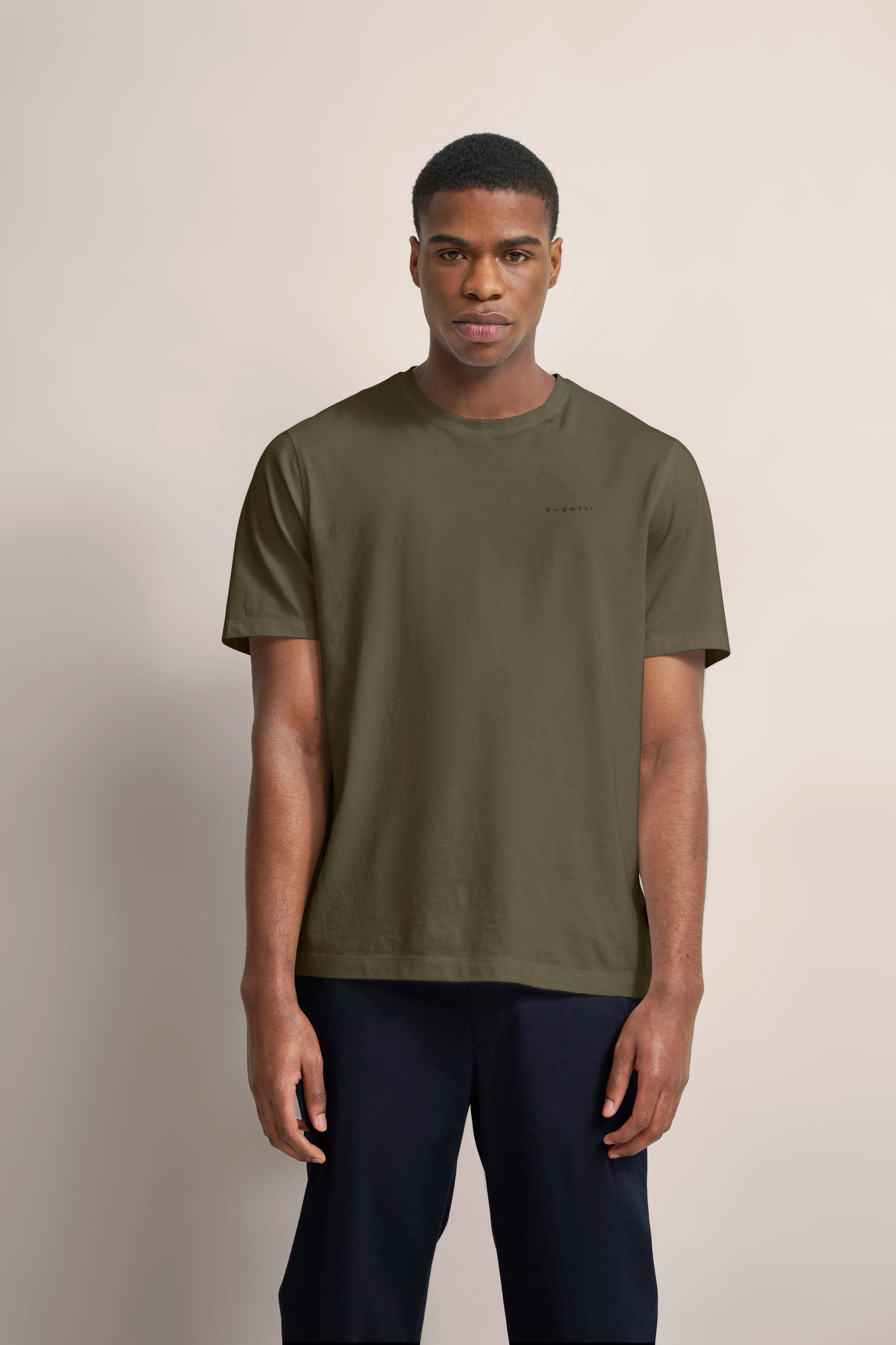 bugatti Modelbild: Olivgrünes T-Shirt, schwarze Hose, entspannte Haltung.
