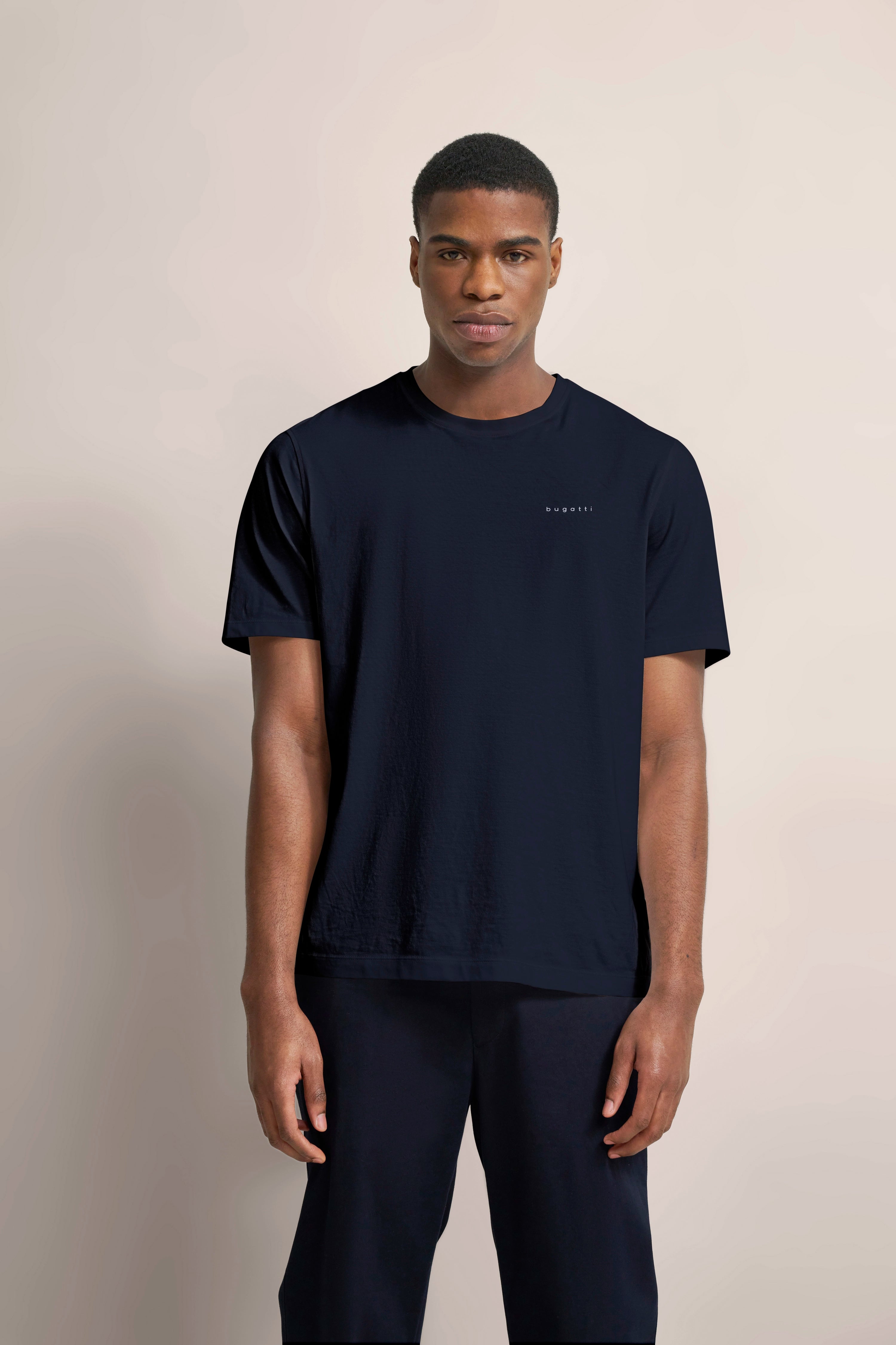 bugatti Modelbild: Mann in navy T-Shirt und Hose, entspannt stehend, minimalistisch und stilvoll.