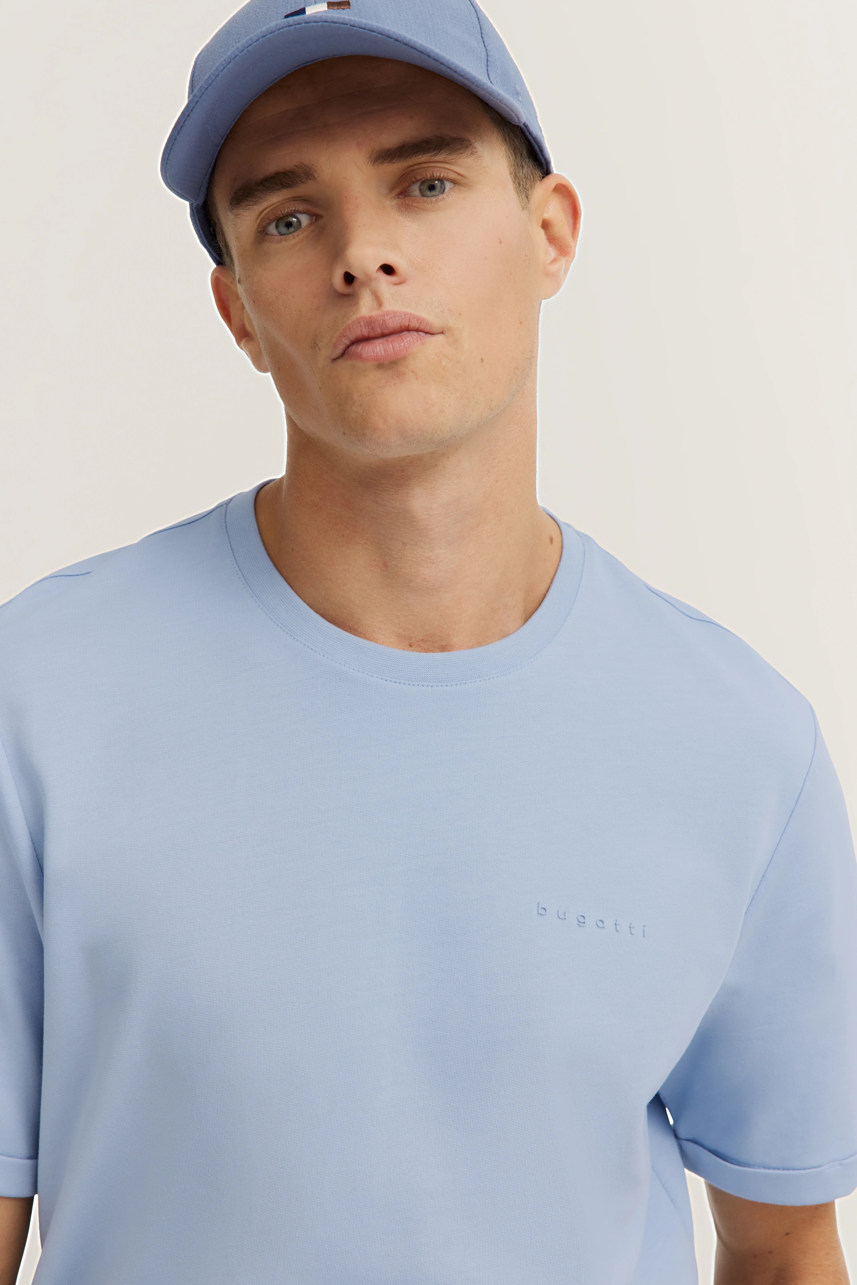 Model in light blue bugatti T-shirt and cap, casual pose, distinctive and stylish.