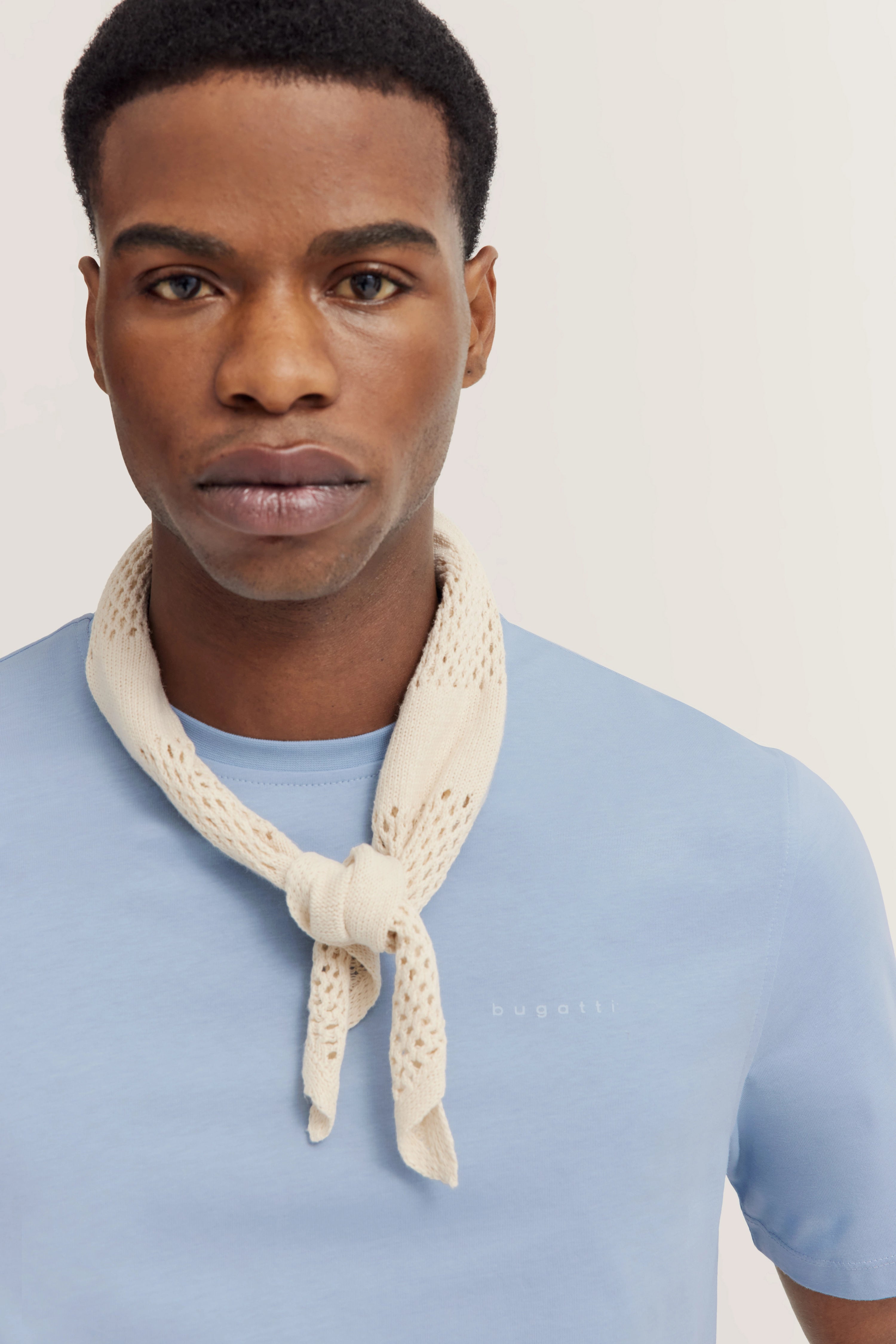 Model trägt hellblaues bugatti T-Shirt mit beigem Strickschal, lässiges Posing.