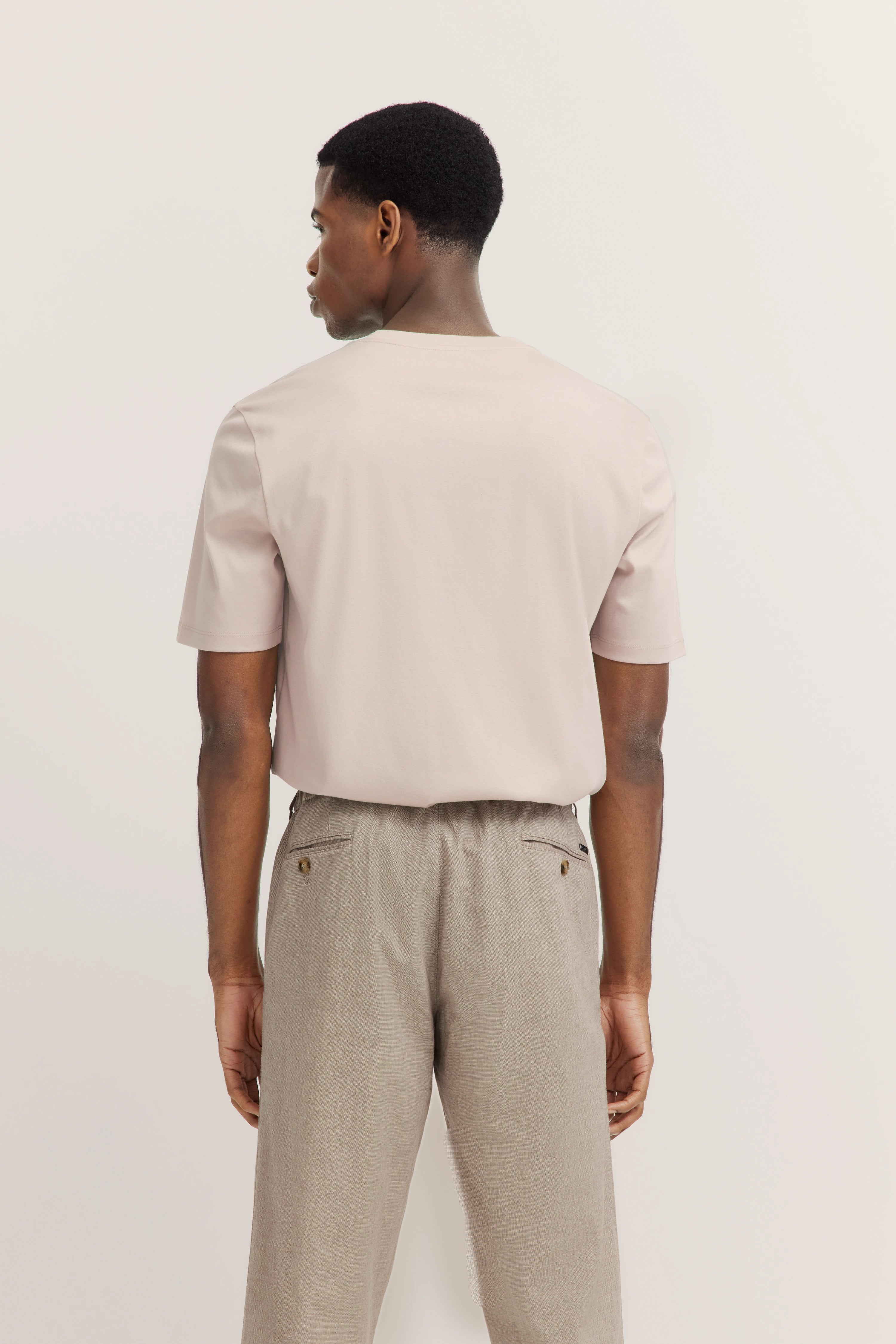 Back view of model in beige bugatti T-shirt and gray pants, casual pose.