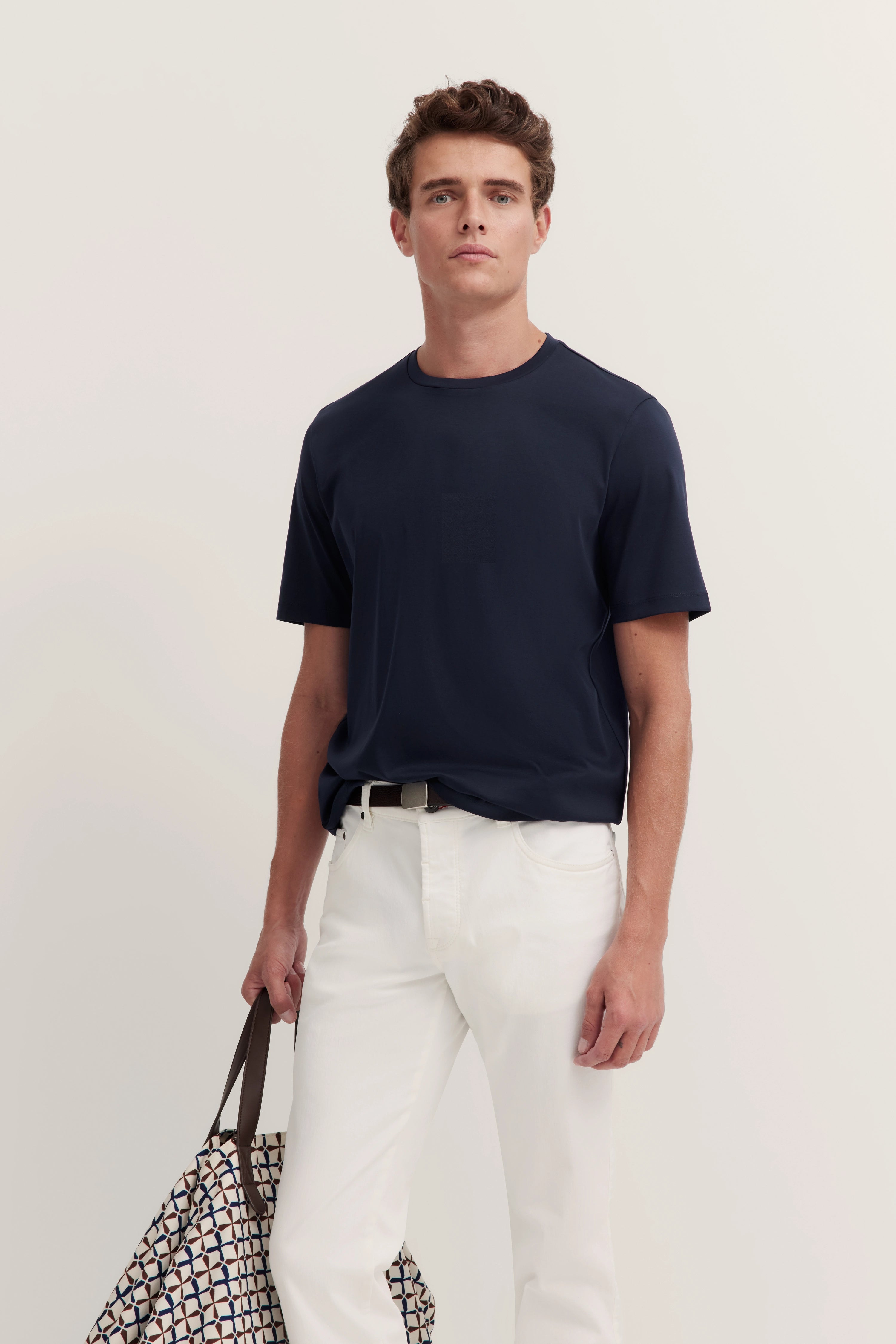 Navy T-shirt and white trousers, model with relaxed look, patterned bag, bugatti style.