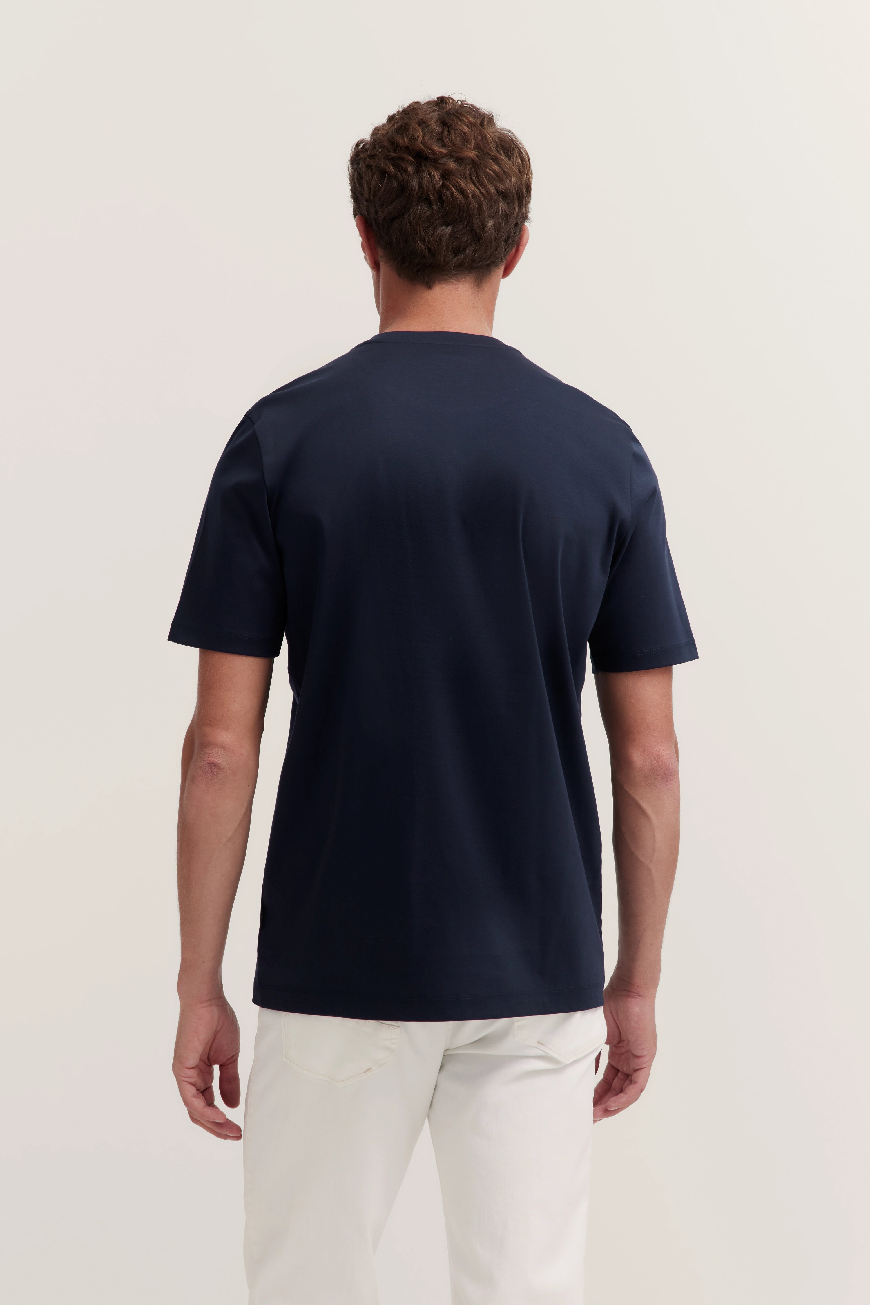 Back view of model in navy T-shirt and white pants by bugatti, casual pose.