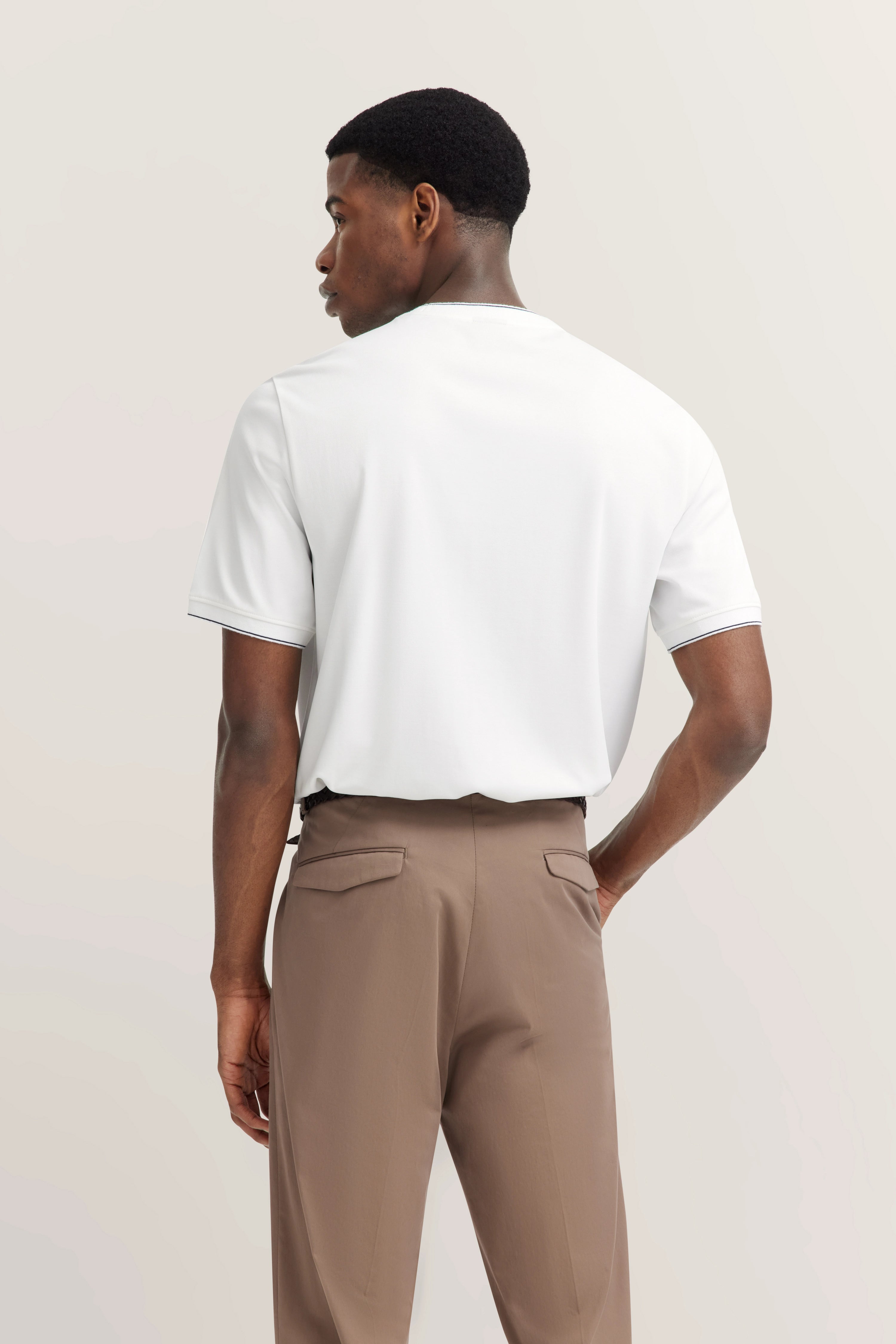 Weißes T-Shirt und beige Hose, Rückansicht Model in legerem Stehen, bugatti Stil.