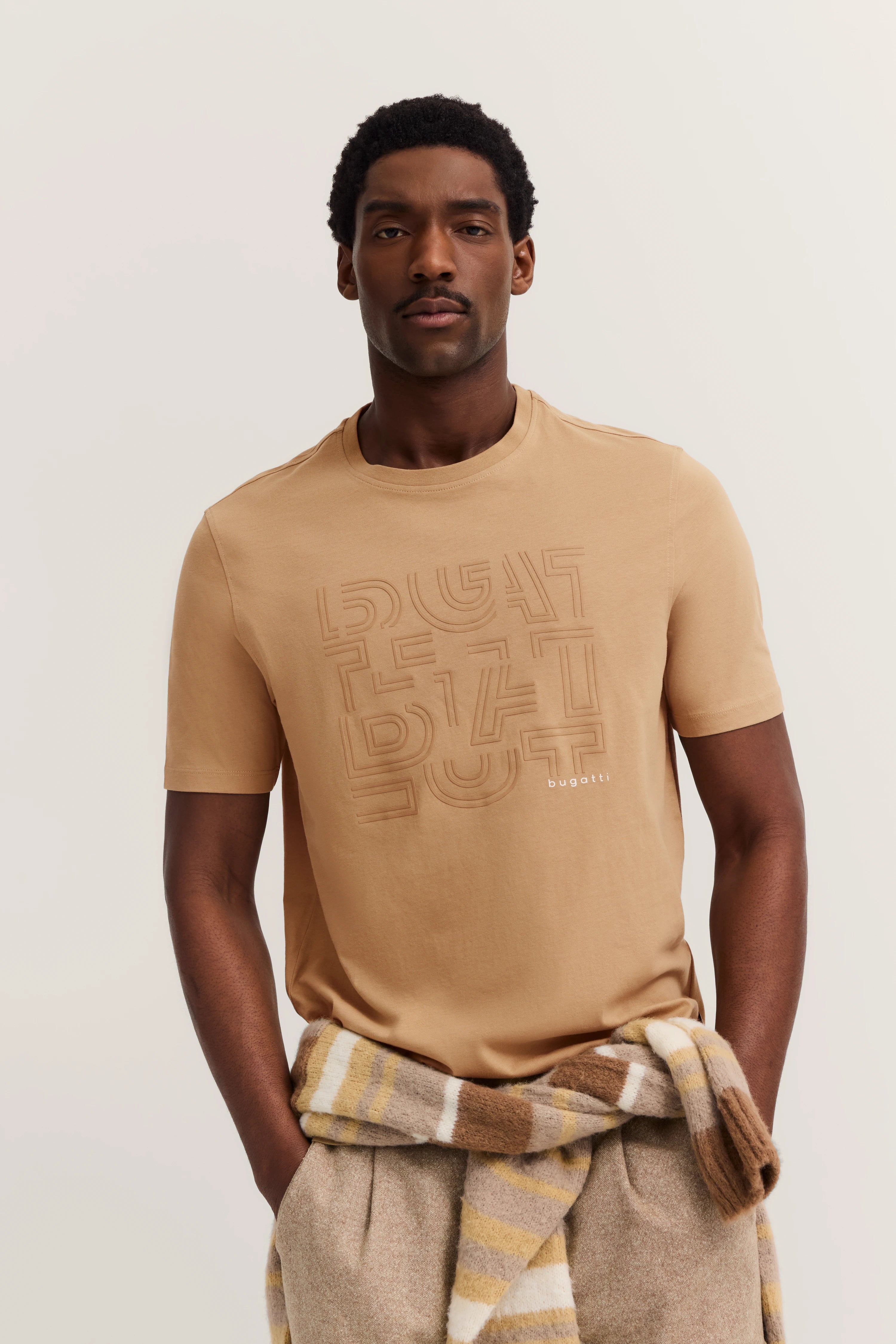 Model in beigem bugatti-T-Shirt, lässig posierend, Pullover um Taille gebunden.