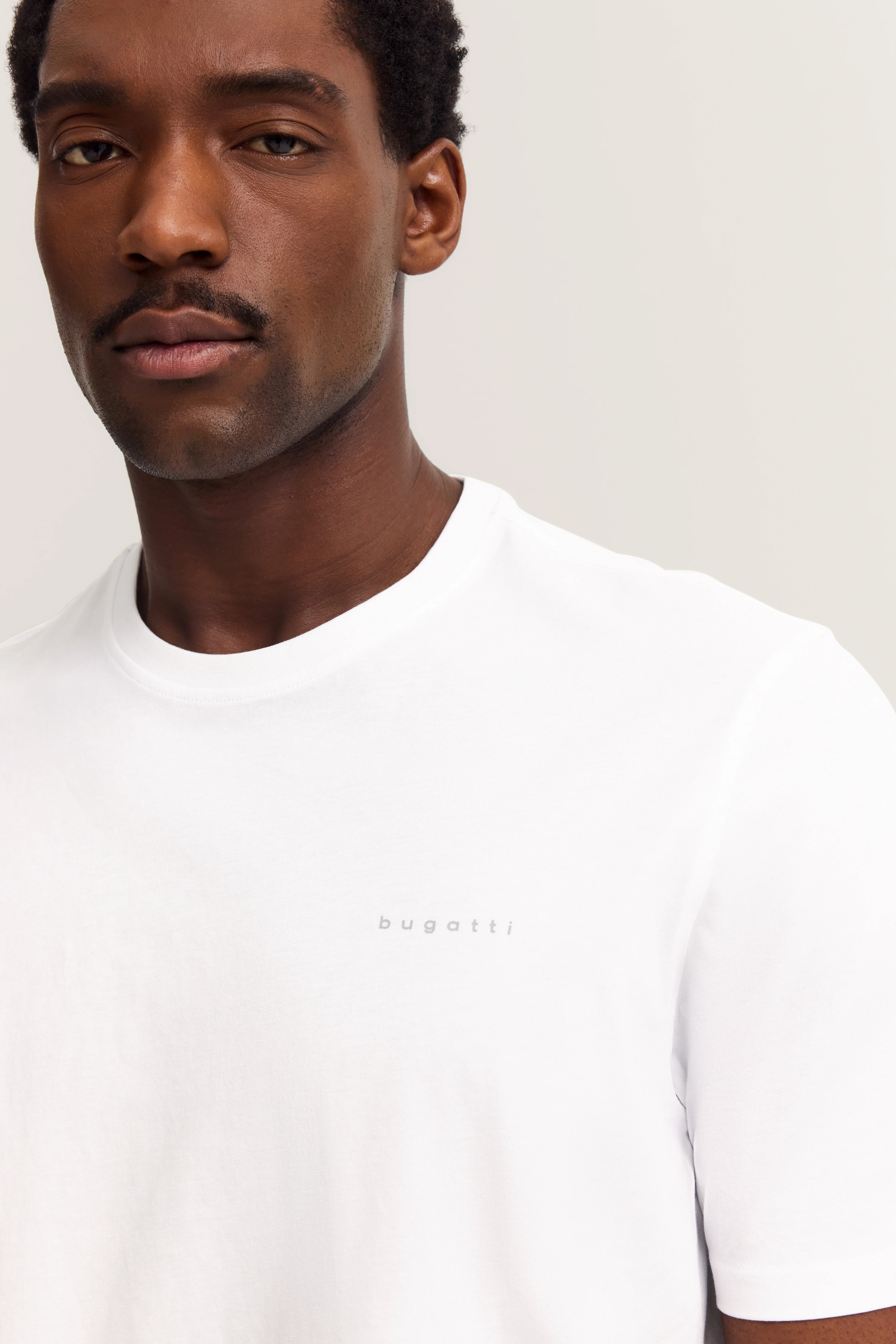 Weißes bugatti T-Shirt, Modelbild, entspannter Blick, minimalistisches Design.