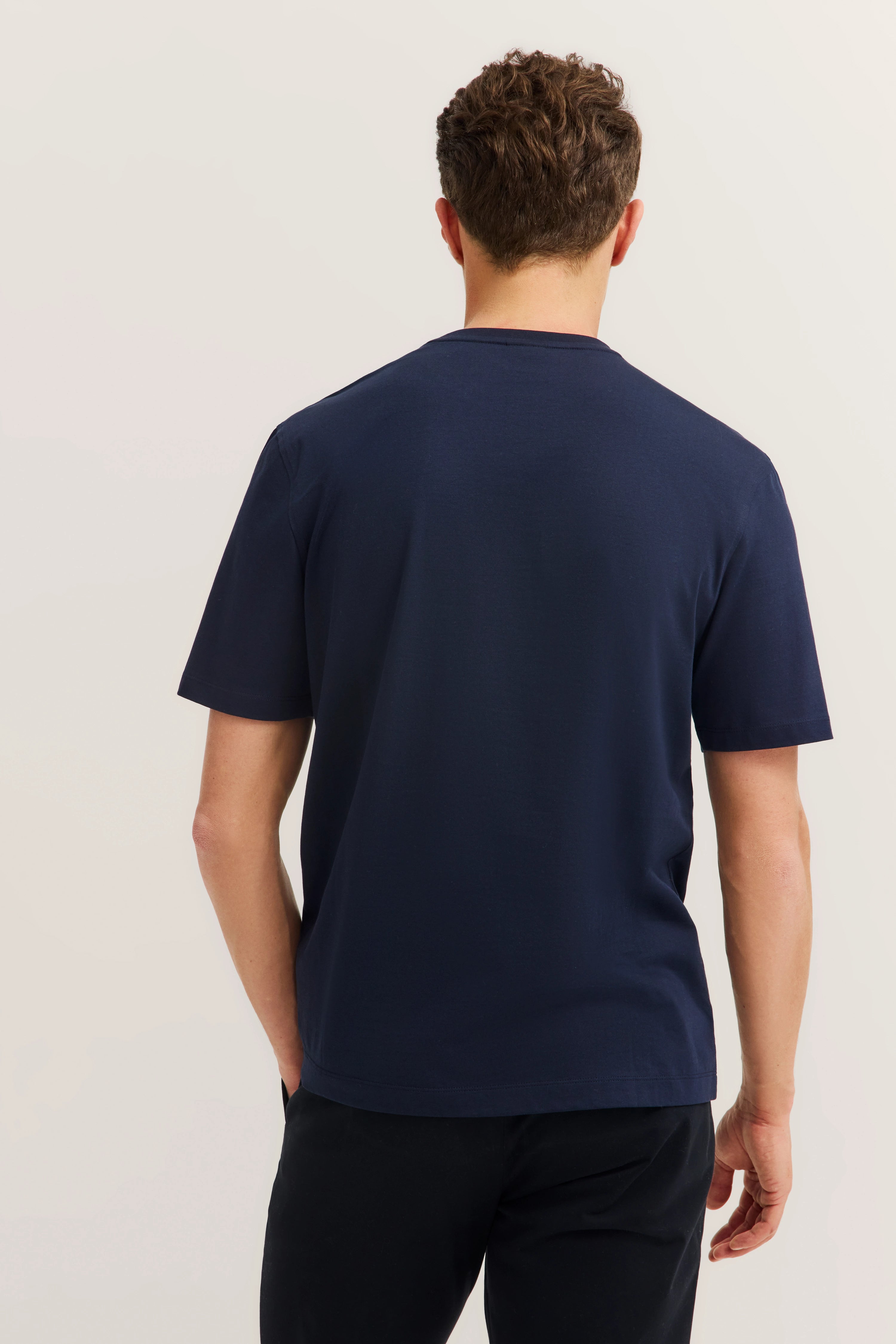 Rückansicht eines Models in navy T-Shirt und schwarzer Hose von bugatti.