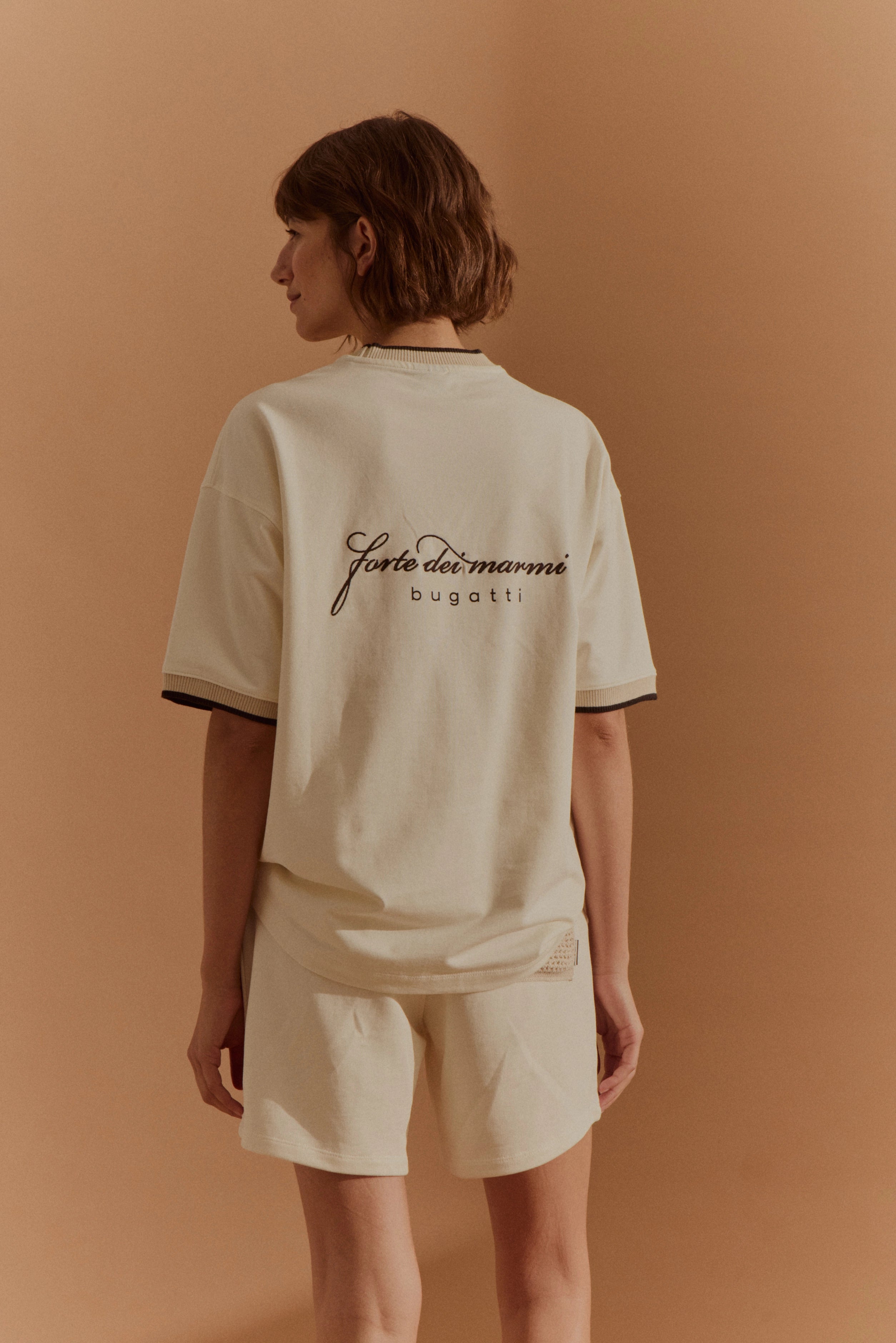 Model in cremefarbenem bugatti Shirt und Shorts, Rückenansicht, entspanntes Posing.