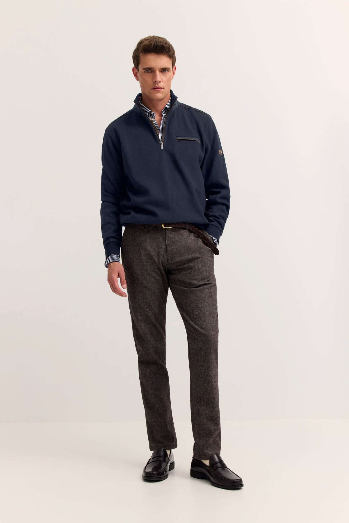 "bugatti Outfit: Modell in dunkelblauem Pullover, grauer Hose, entspannt stehend."