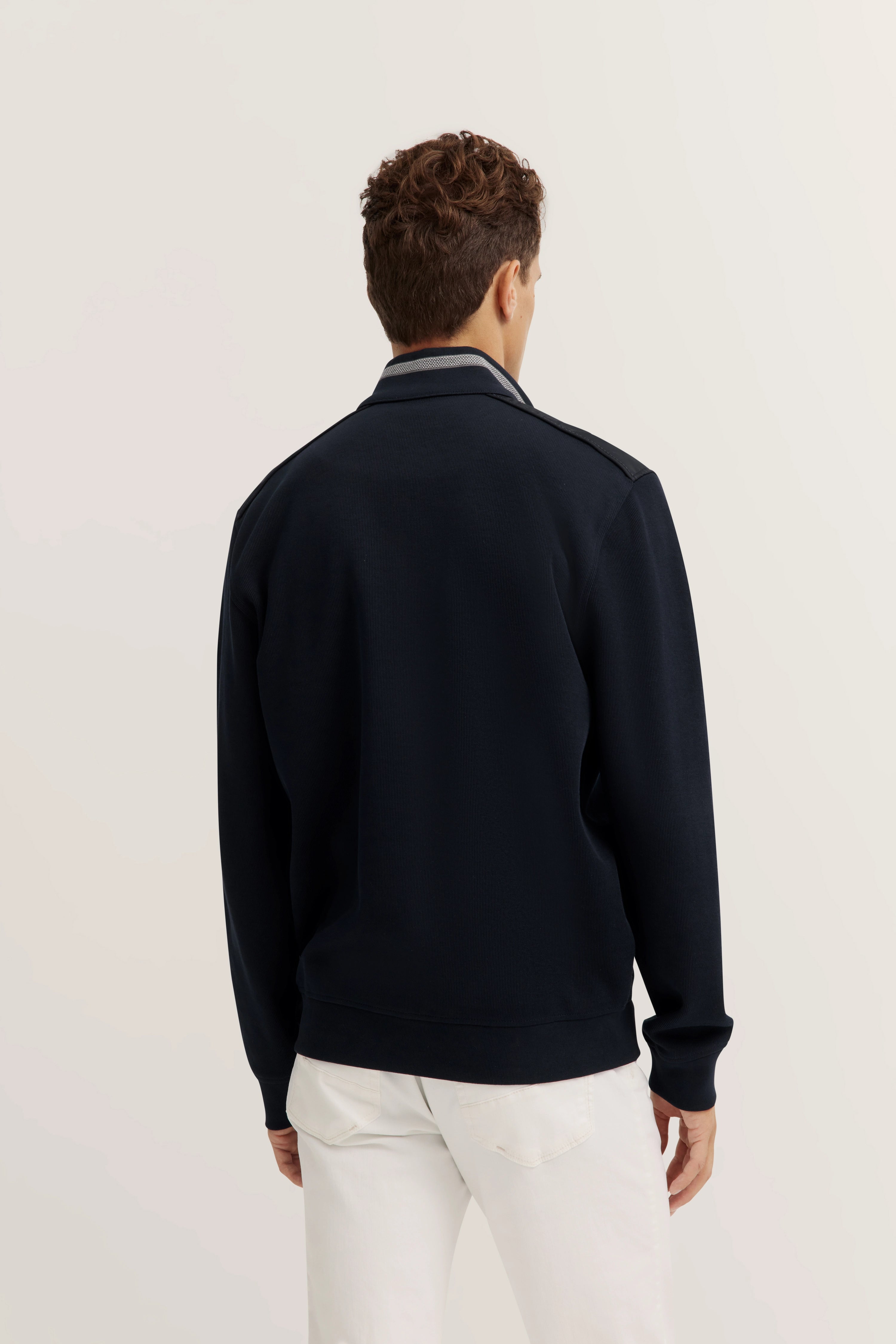 bugatti Modelbild, Rückenansicht, dunkelblauer Pullover, weißer Jeans, lässige Pose.