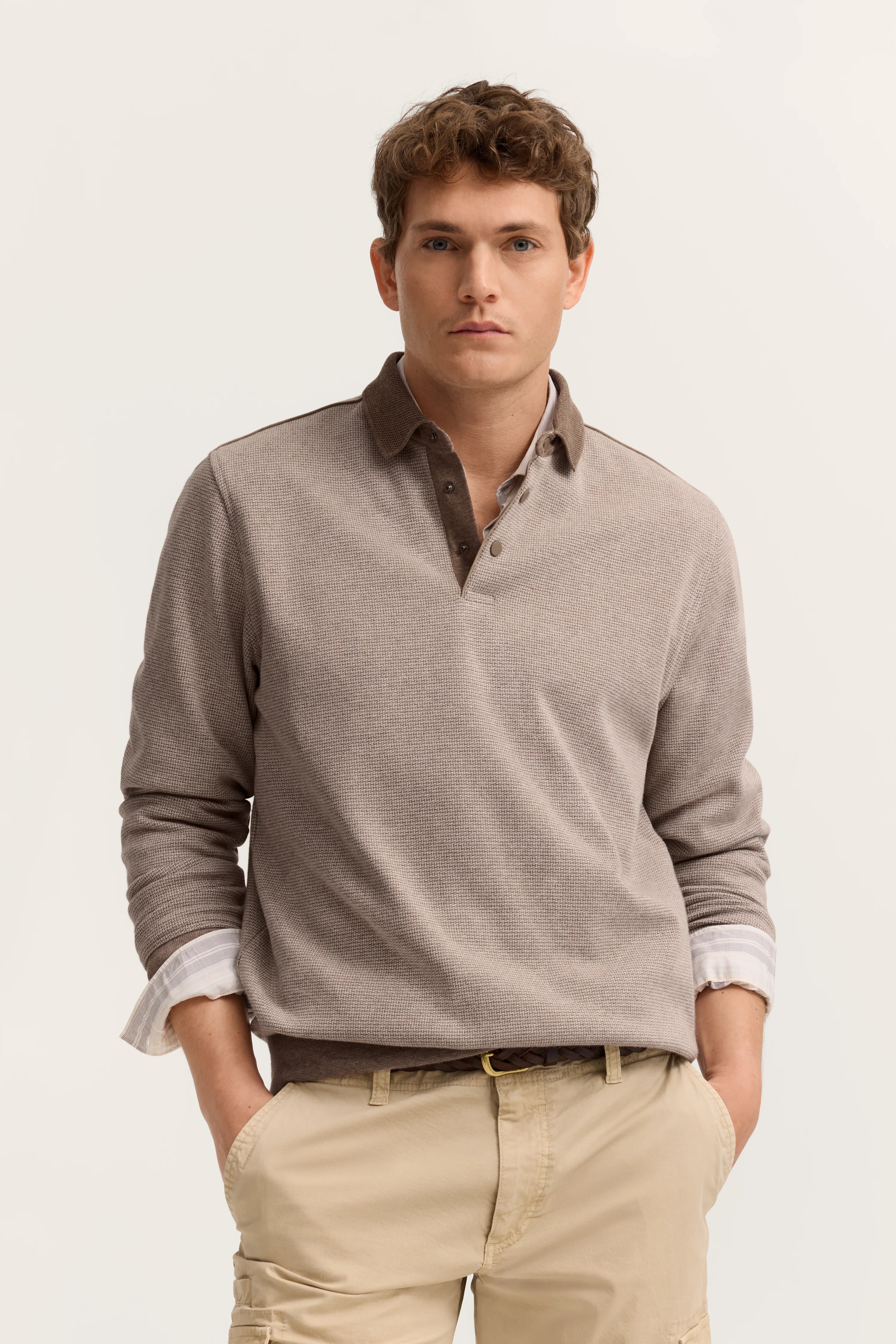 Bugatti Modelbild: Beiges Polo-Shirt über weißem Hemd, lässige Pose mit Händen in der Hosentasche.