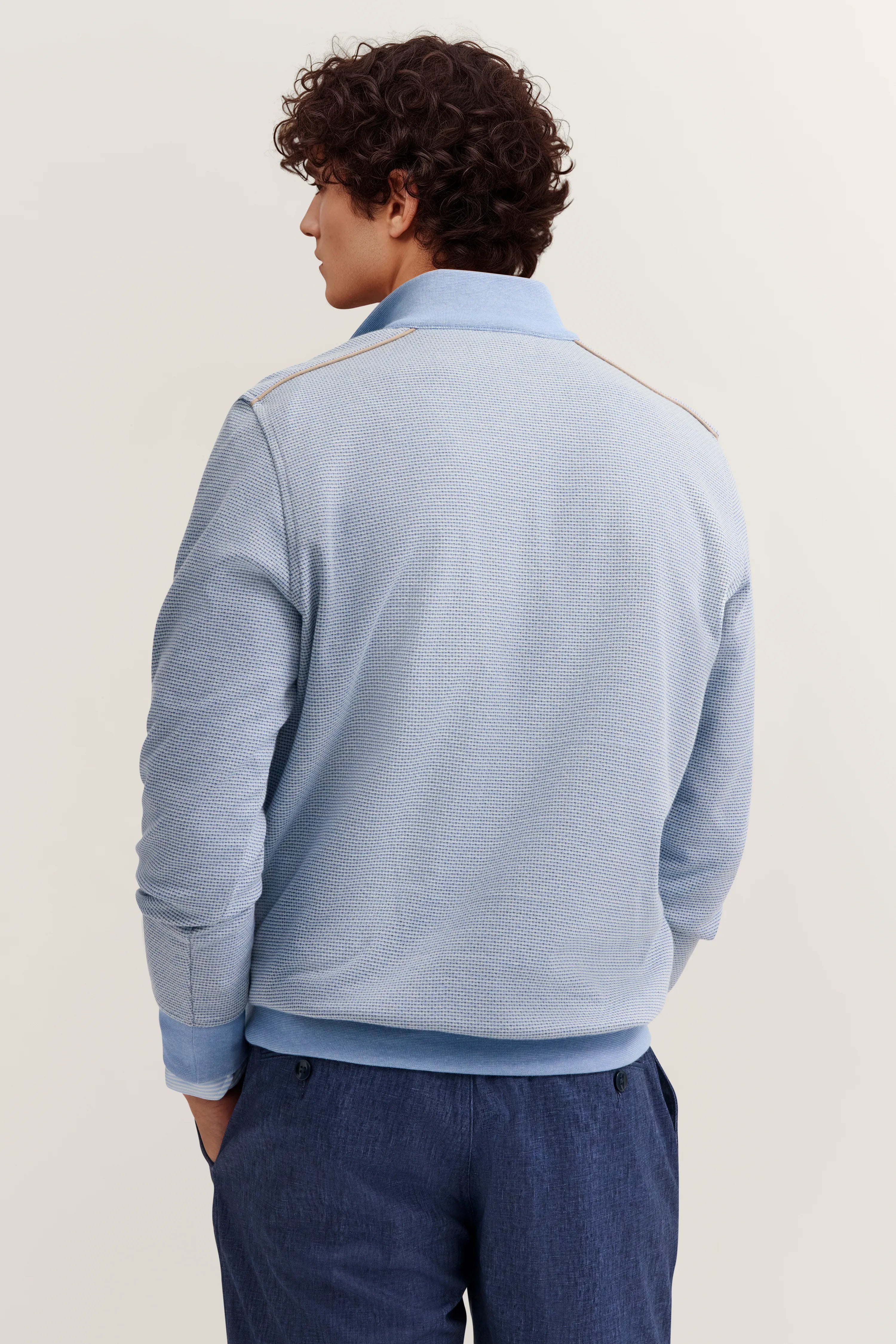 Model trägt hellblauen bugatti Pullover, freizeitlich, mit blauen Hosen, entspannte Pose von hinten.