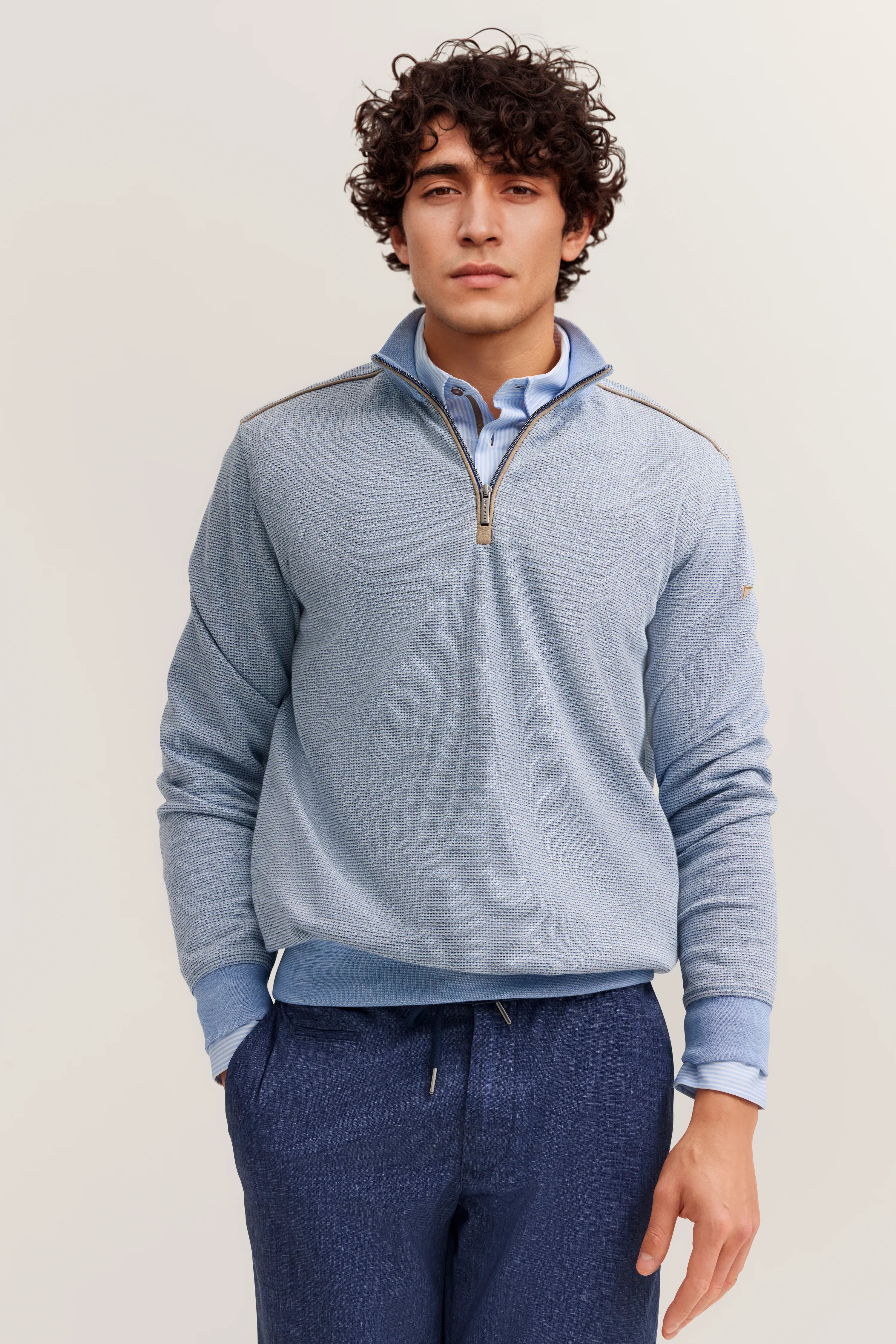 bugatti Model im hellblauen Pullover und blauer Hose, legeres Posing, entspannter Stil.