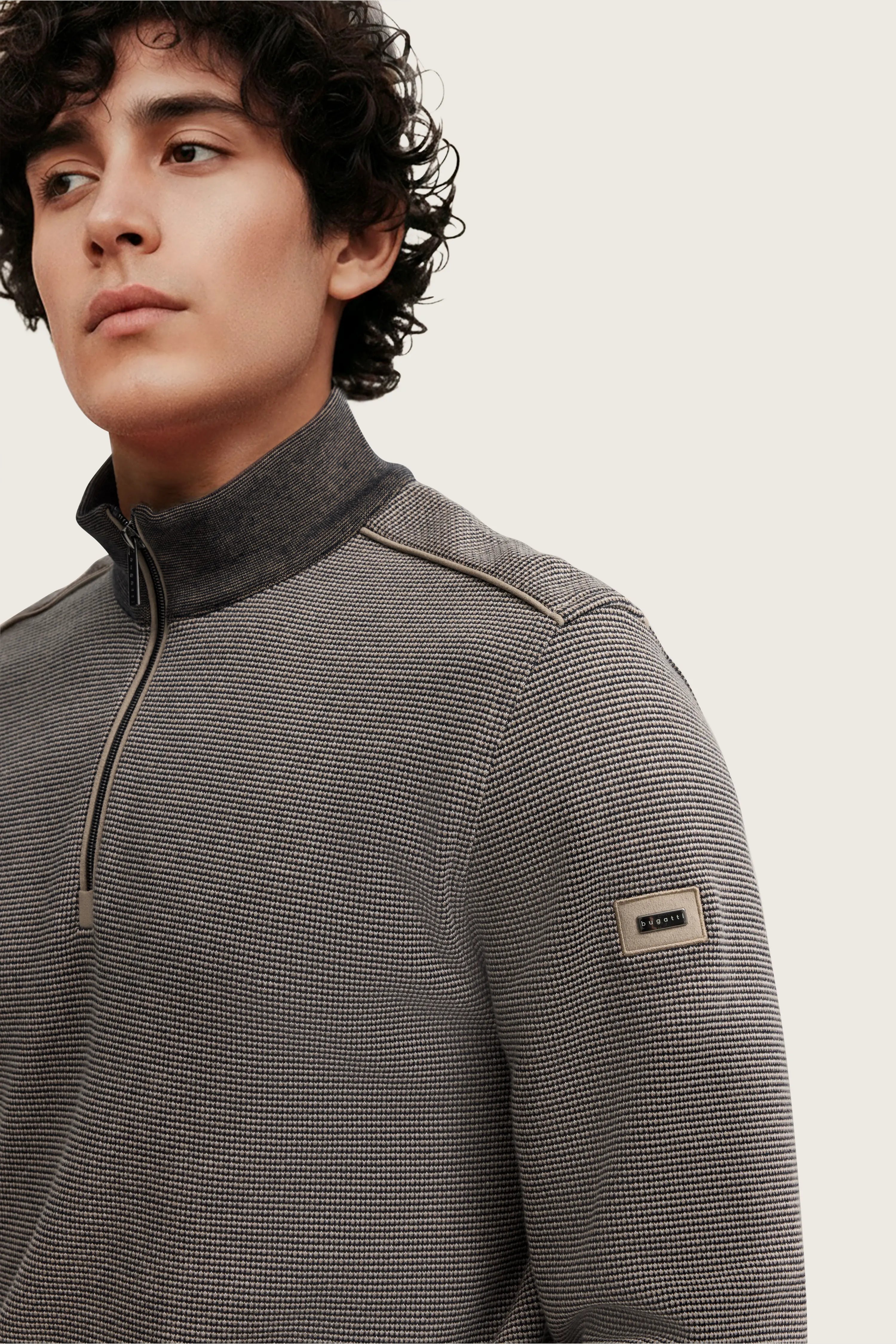 Bugatti Modelbild, Mann trägt grauen Pullover mit Stehkragen, dezentes Muster, entspanntes Posing.