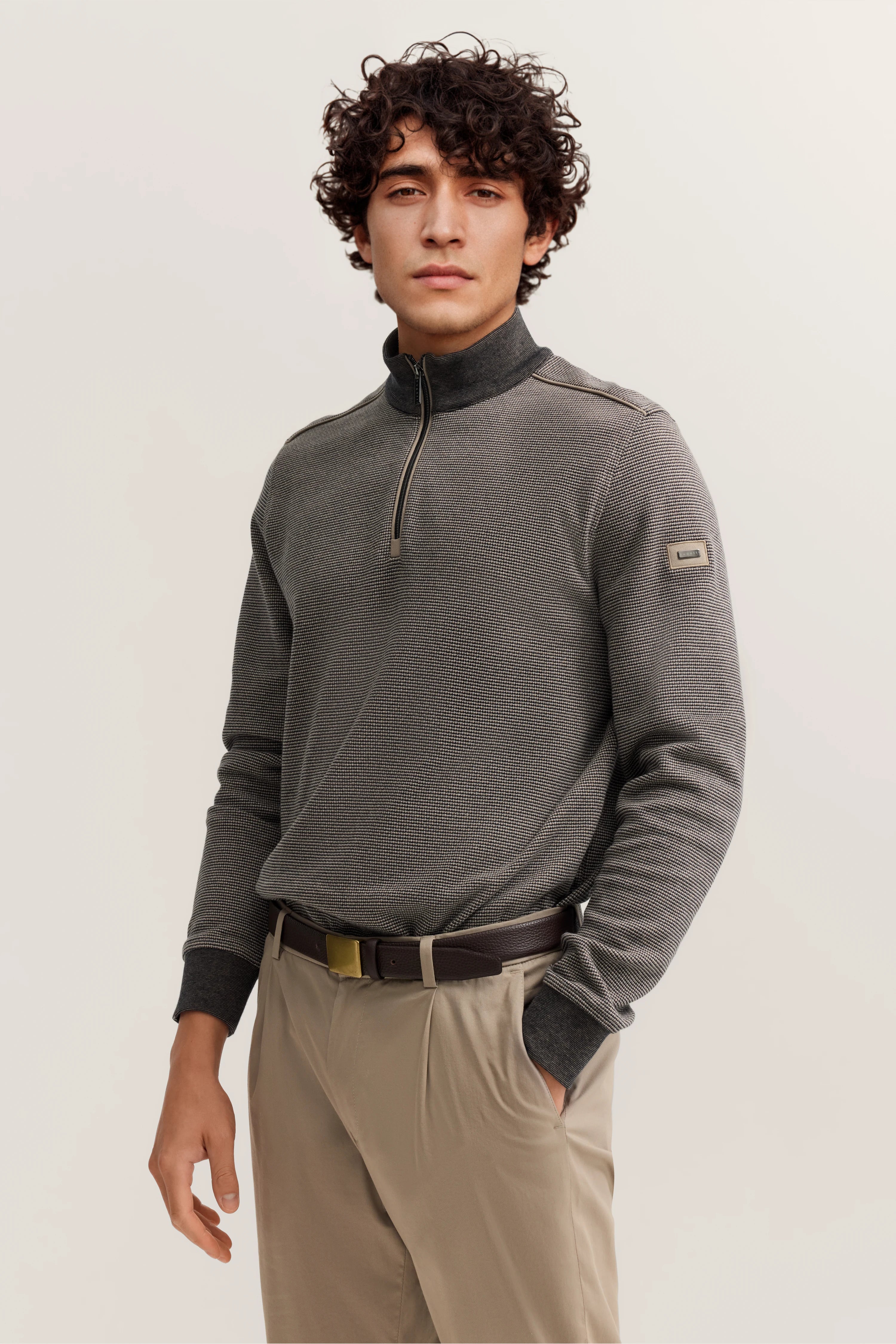 Graues bugatti Pullover Modelbild, beige Hose, lässiges Posing, Hand in Tasche.