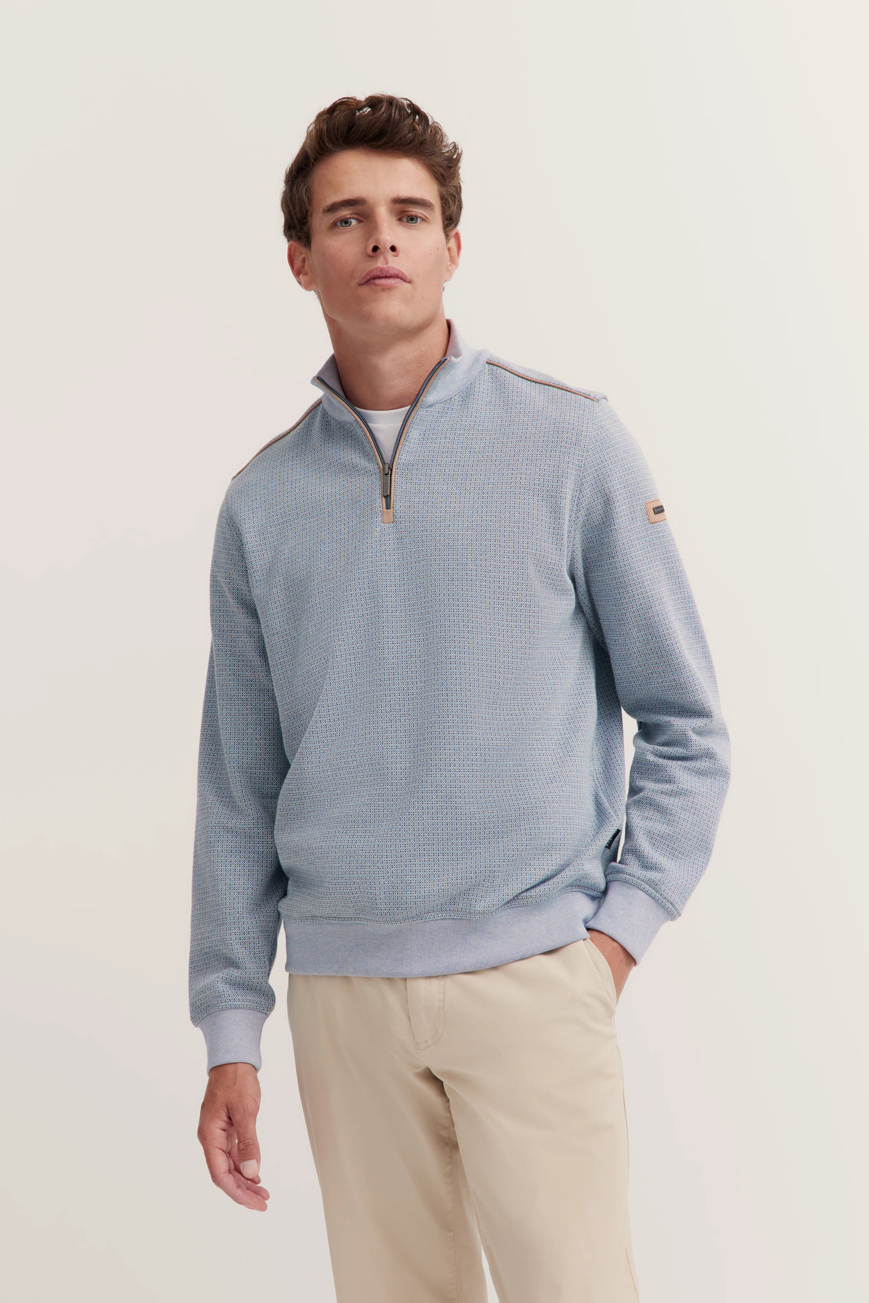 Elegante lichtblauwe pullover met rits, gecombineerd met beige broek, gemodelleerd in ontspannen pose.