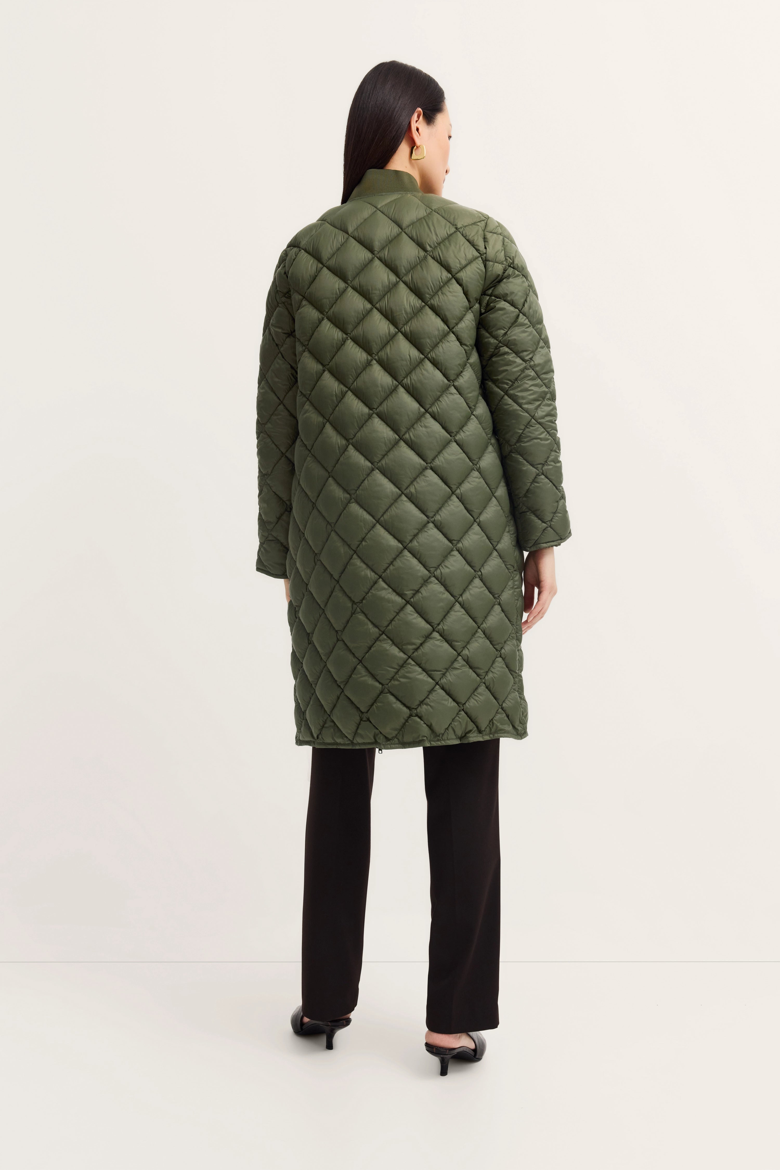 Green quilted bugatti coat, model from behind, black pants, relaxed pose.