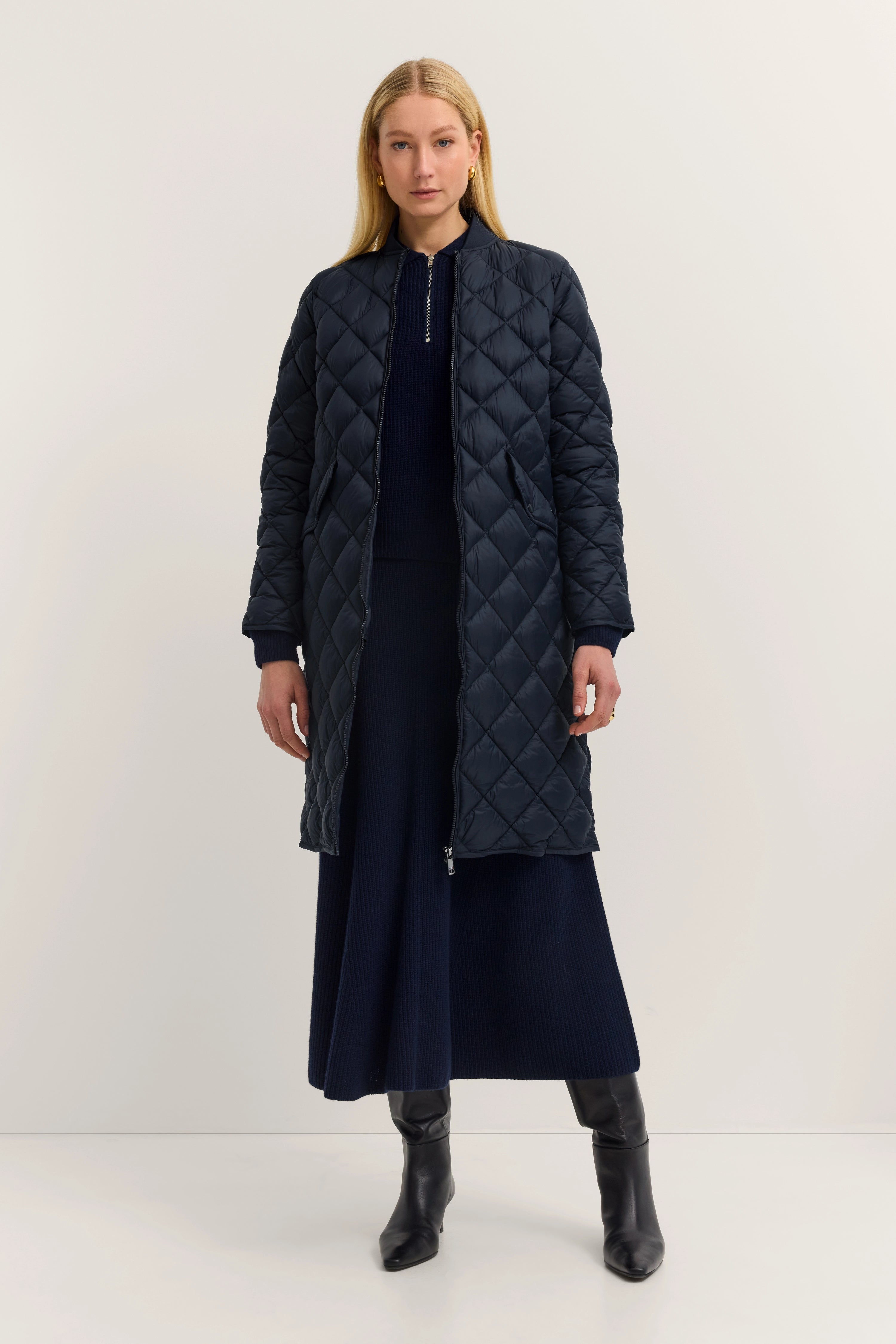 Model in long, quilted, dark blue bugatti coat, elegant pose, matching outfit.
