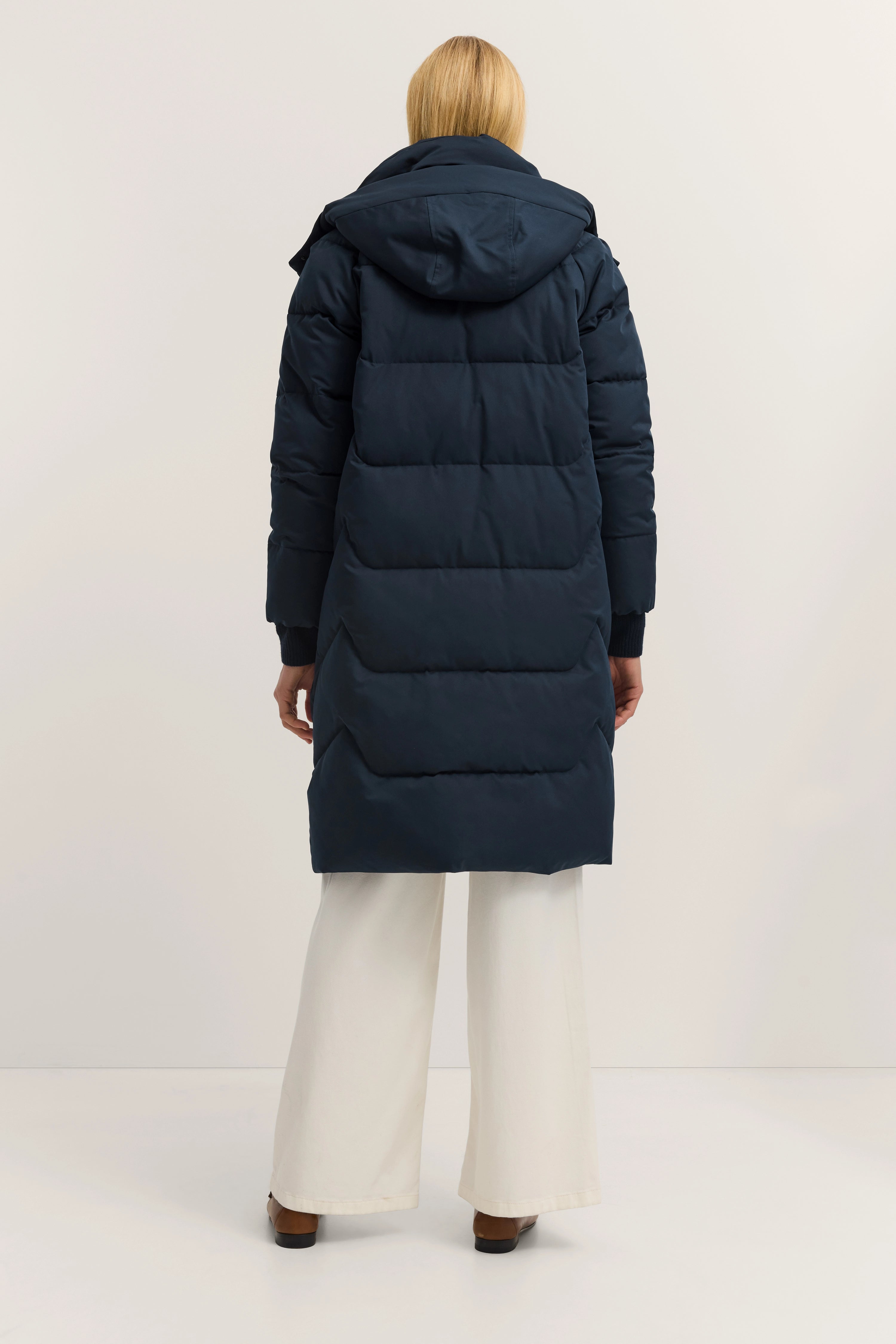 Donkerblauwe bugatti donsjas, model van achteren, witte broek, casual look.