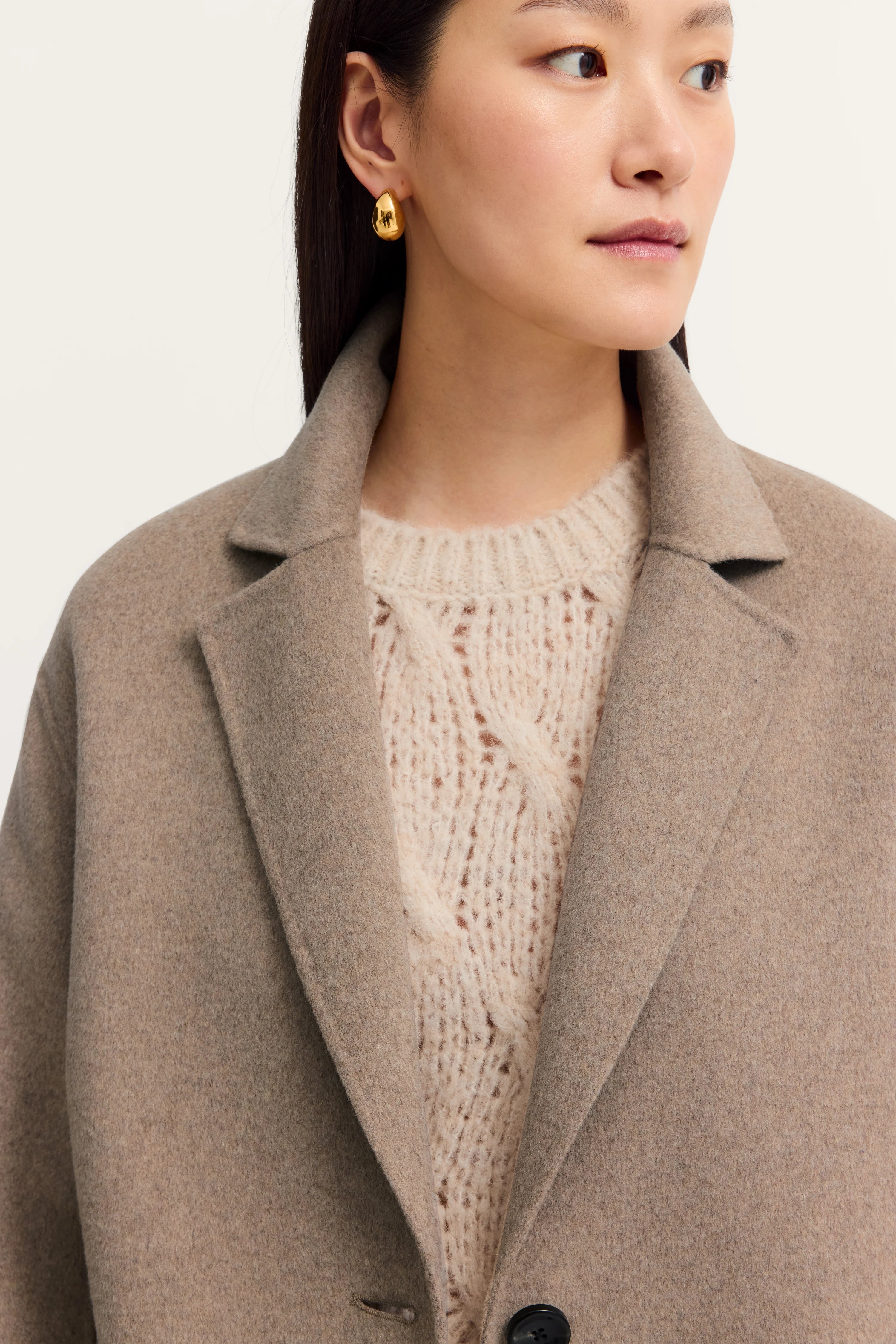 Beigefarbener Mantel und cremefarbener Strickpullover, Modelbild seitlich.