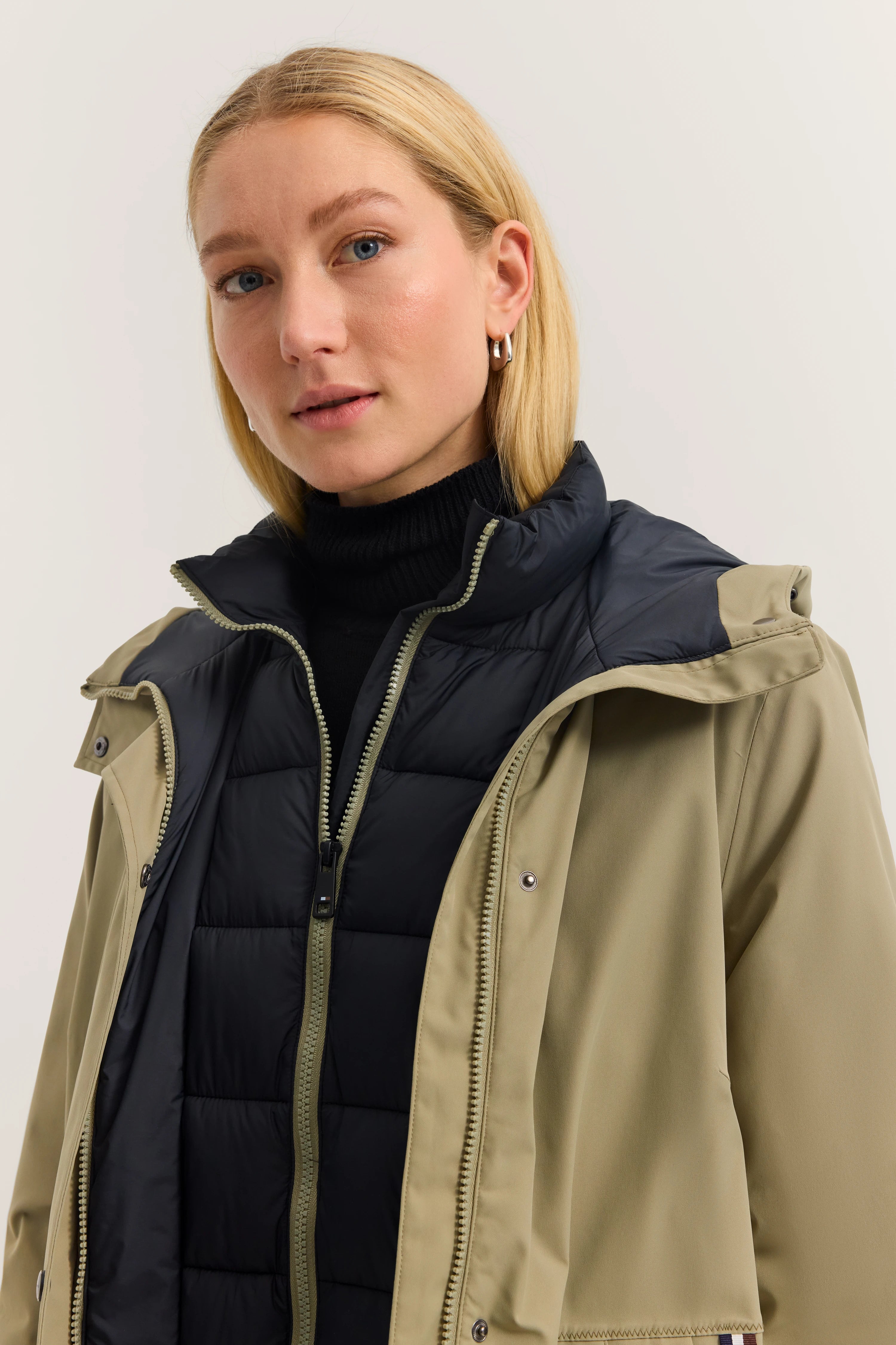 Blondes Model trägt schwarze Steppweste und olivgrüne Jacke von bugatti, legeres Büstenbild.