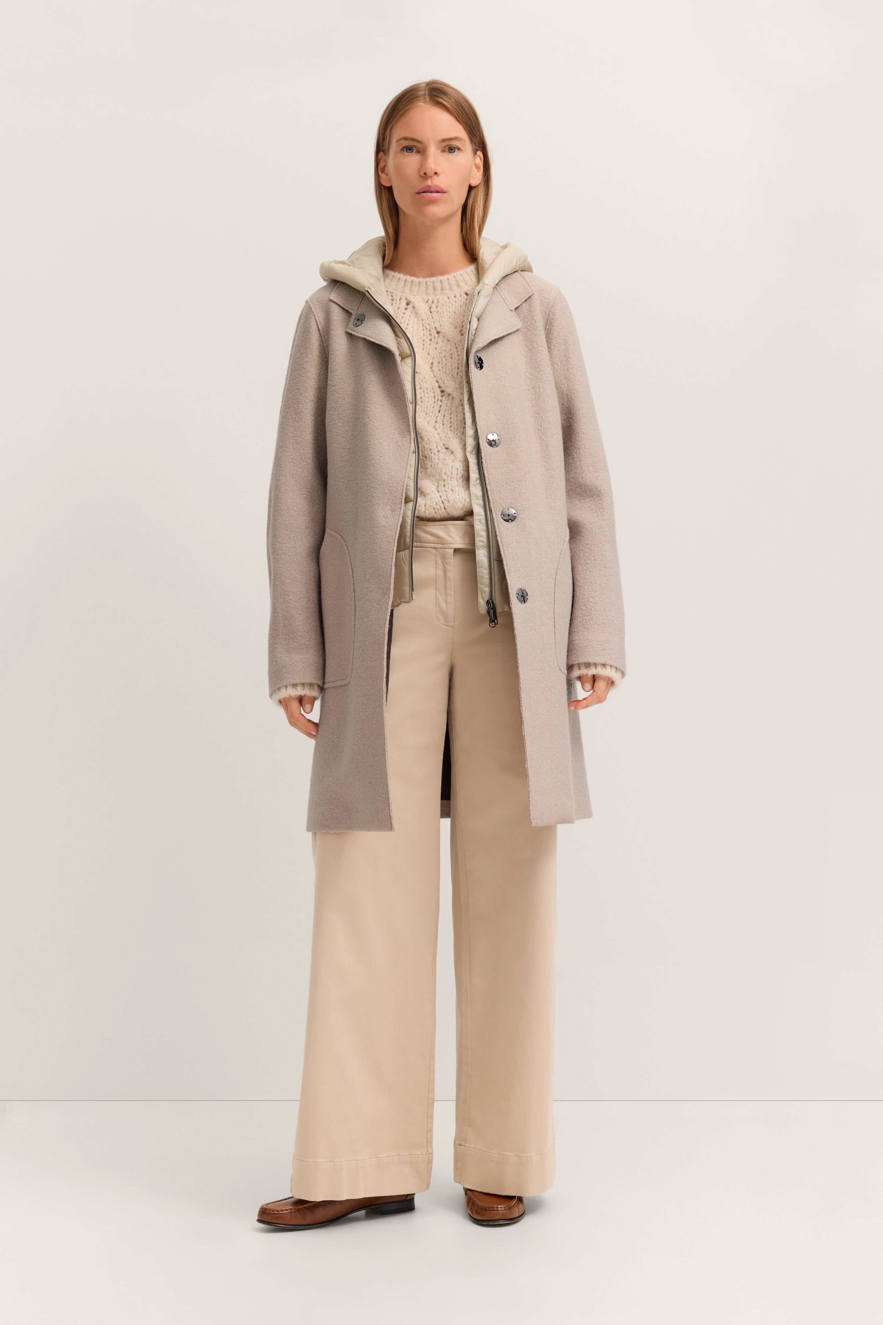 Beige bugatti Mantel mit Strickpullover und weiten Hosen. Modell steht frontal, entspannter Ausdruck.
