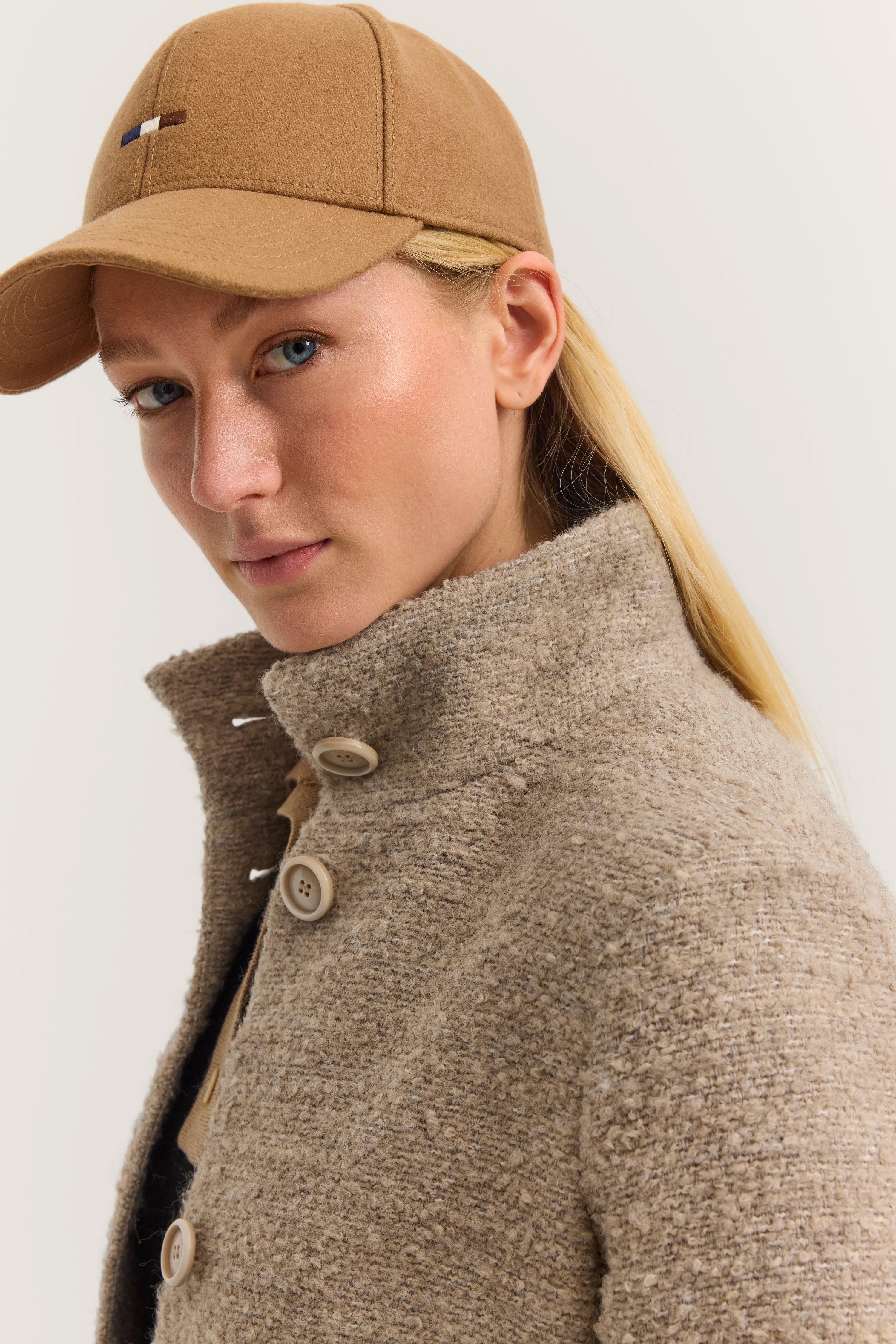 Model met beige bugatti muts en jas, halfprofiel pose.
