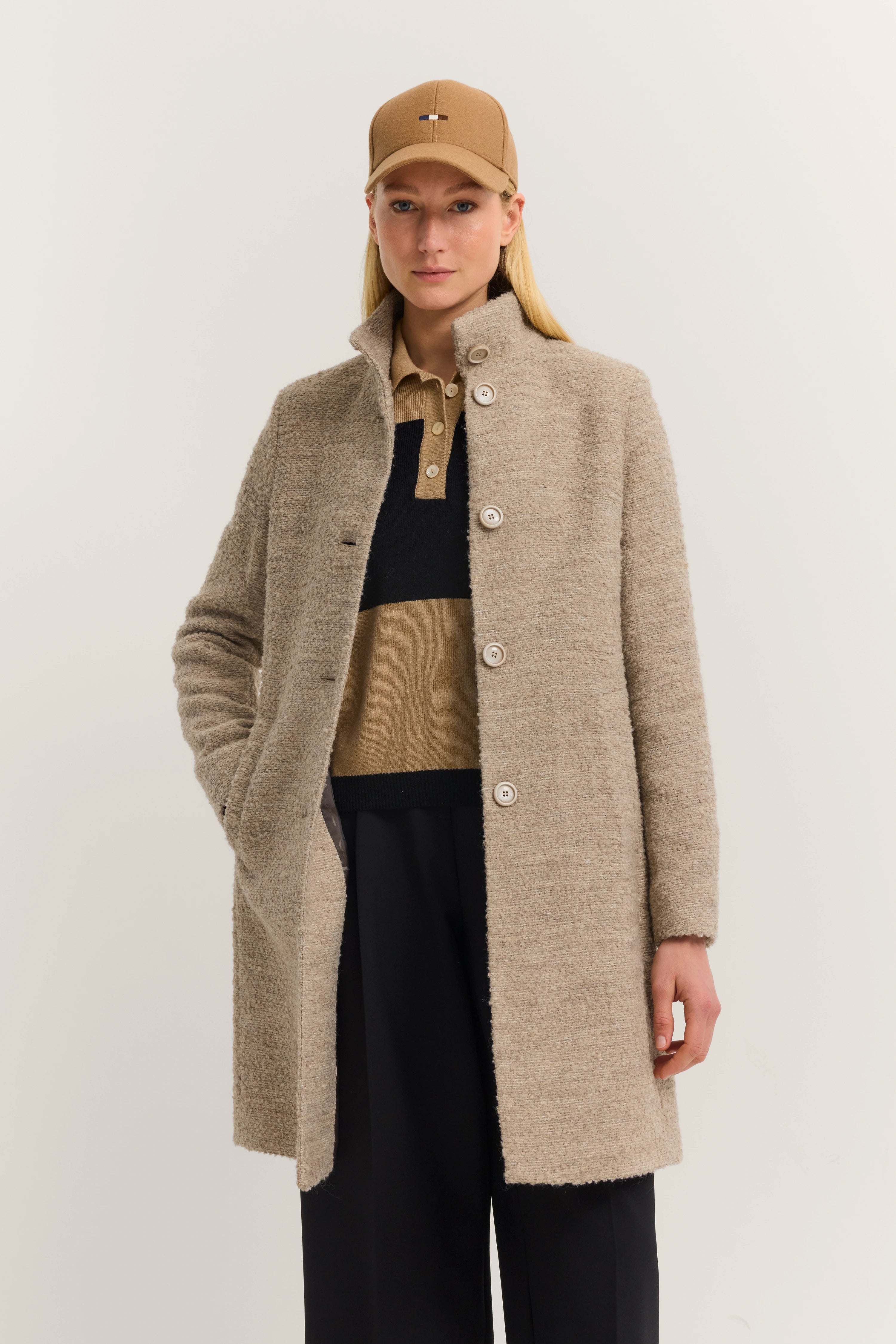 Model draagt beige bugatti-jas, zwarte broek en beige pet, ontspannen pose.