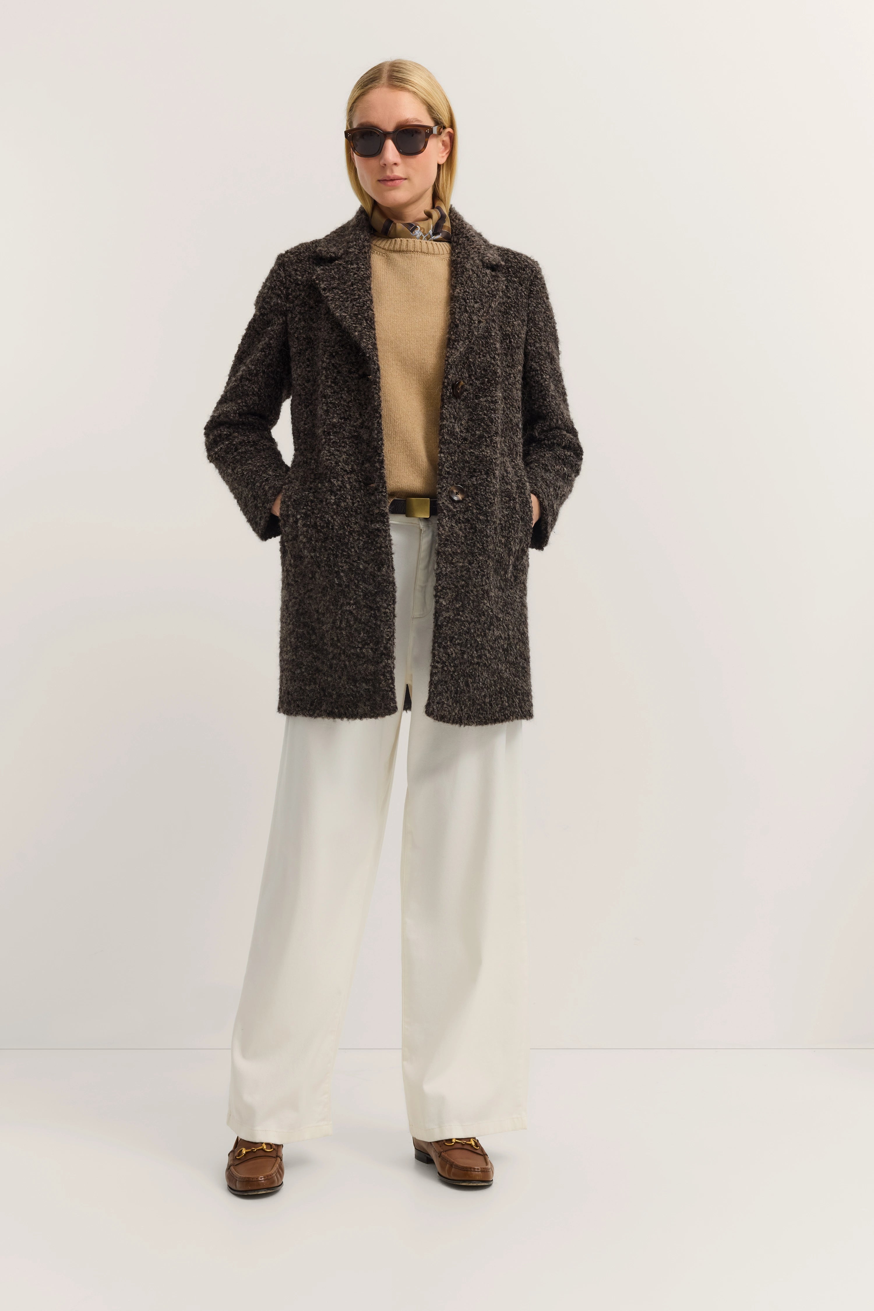Model draagt bruine jas, beige trui, witte broek