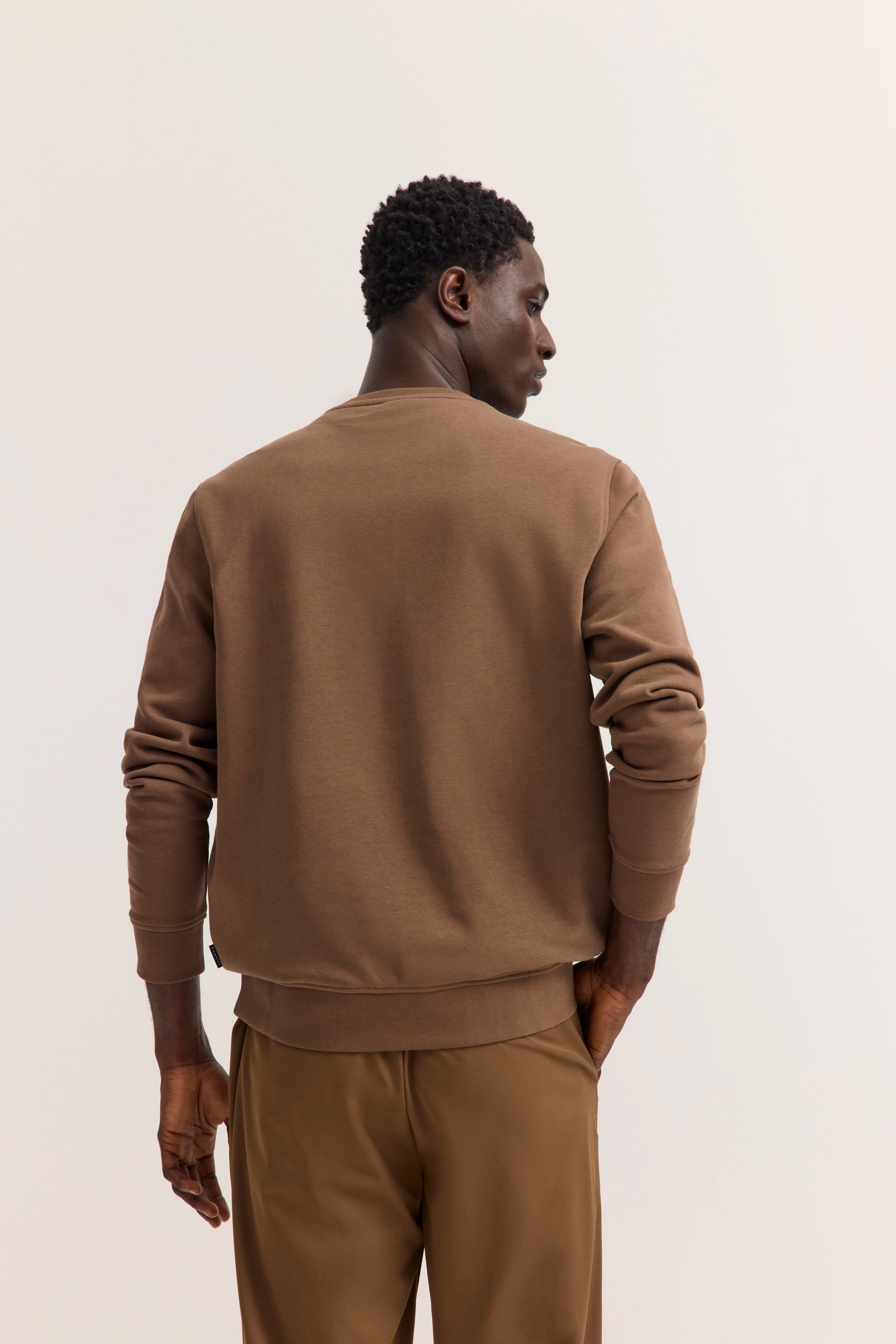 Braunes Sweatshirt und Hose, Rückenansicht, legeres Modelbild, entspannte Haltung.
