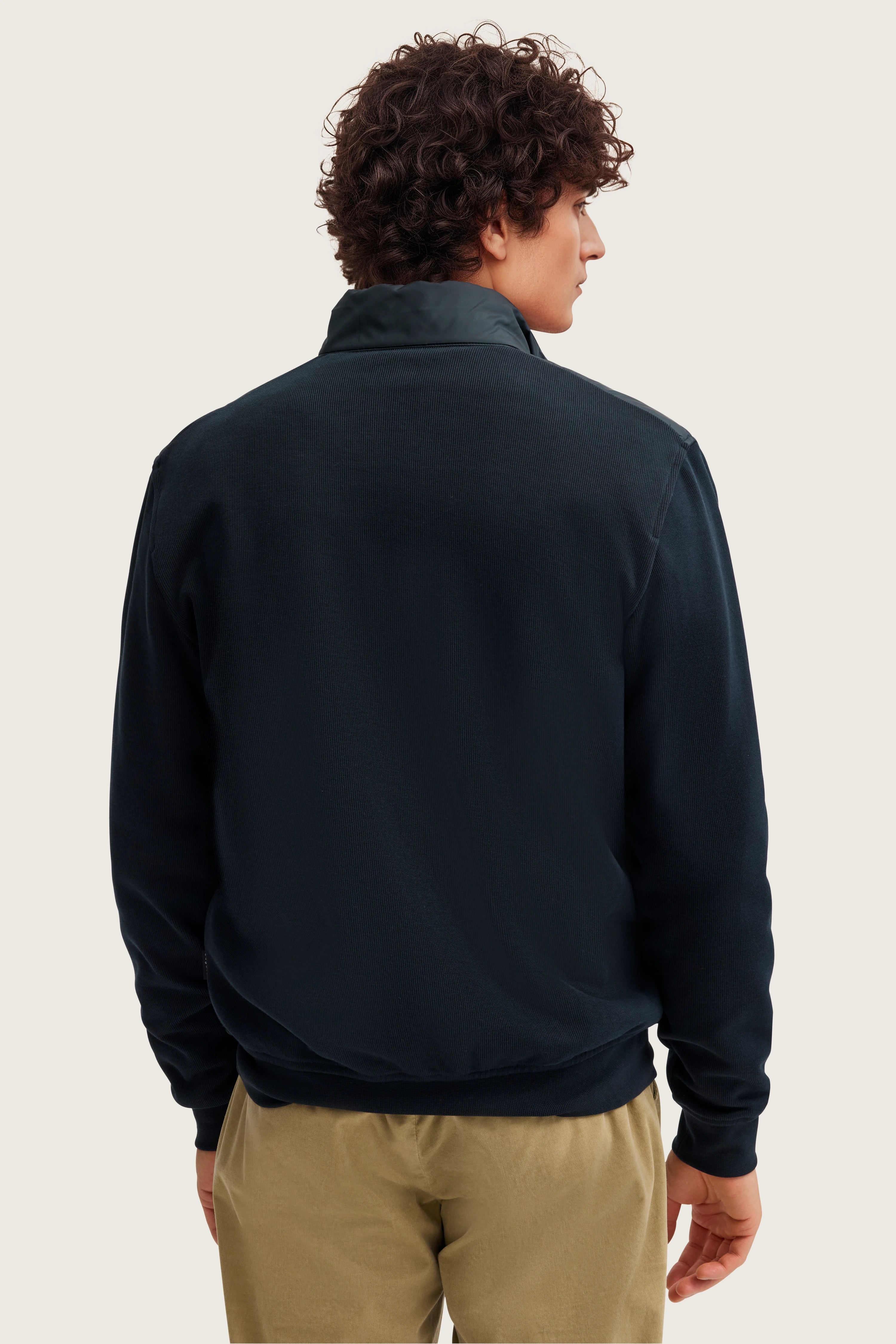 Rückansicht Model in schwarzem bugatti Pullover, beige Hose, entspannte Haltung.