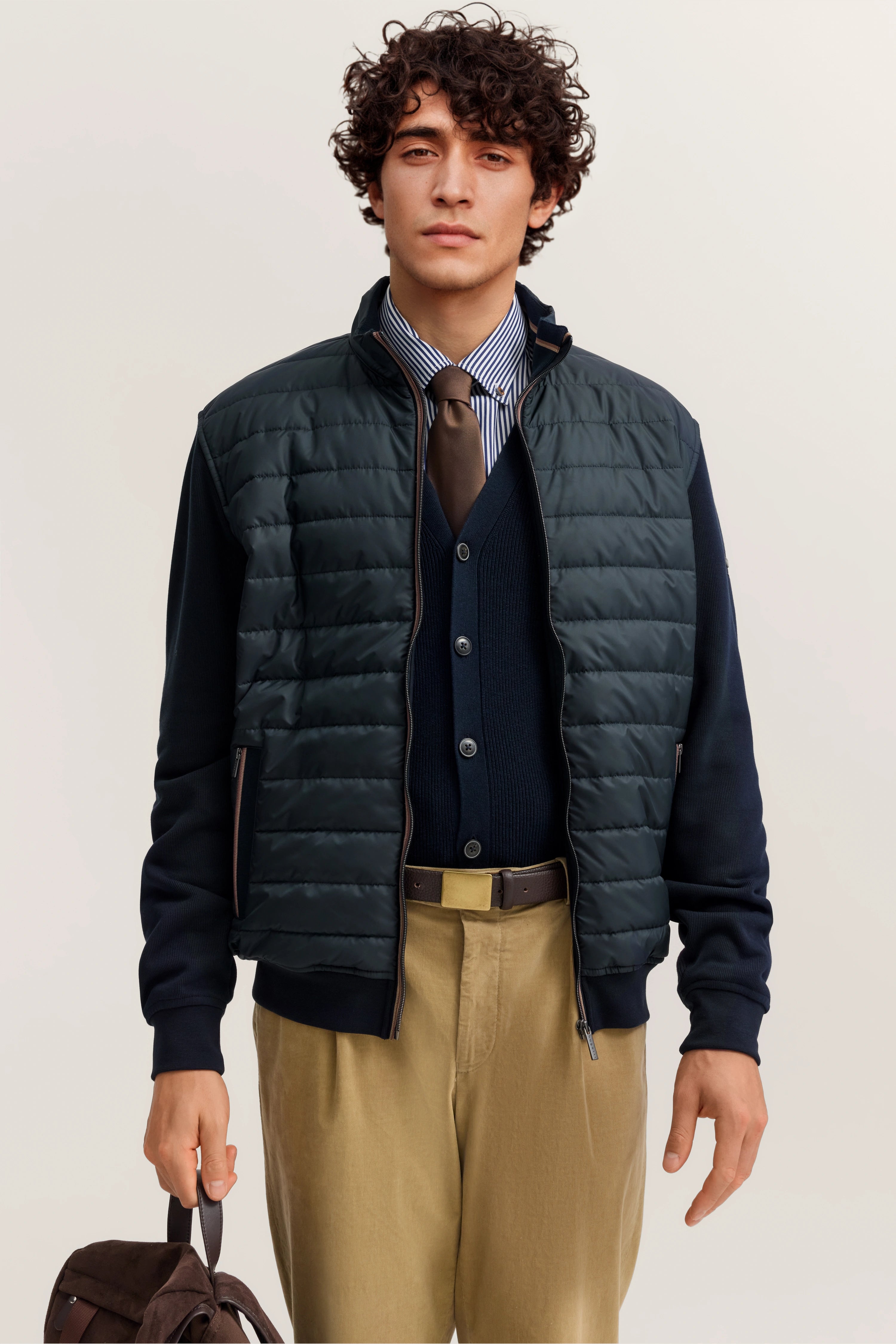 Model in gestepptem, dunkelblauem bugatti Blouson, gestreiftem Hemd, Krawatte und beige Hose.
