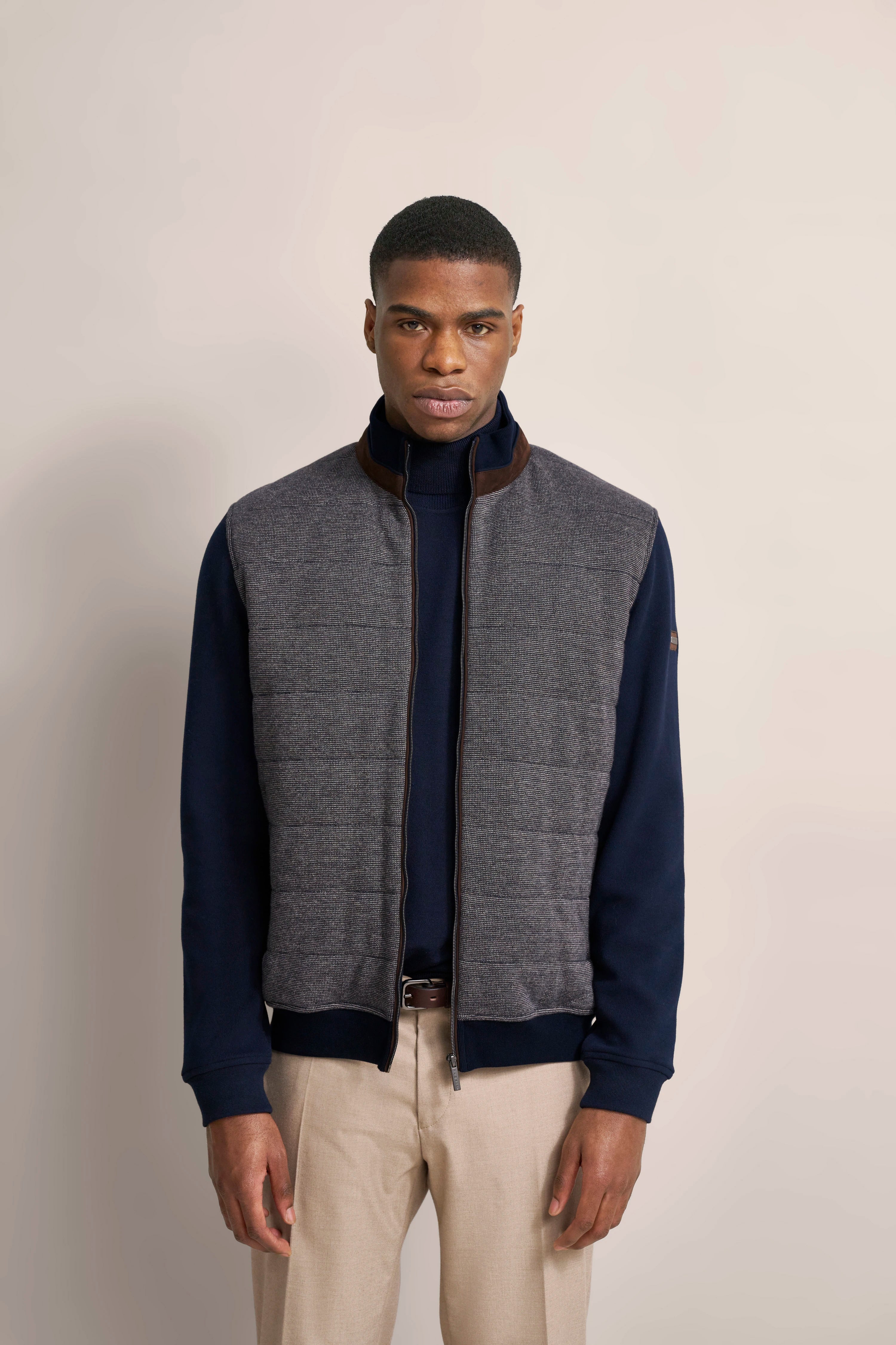 Graue Weste mit Steppmuster, marineblauer Pullover, beige Hose, Modelbild, frontales Posing.